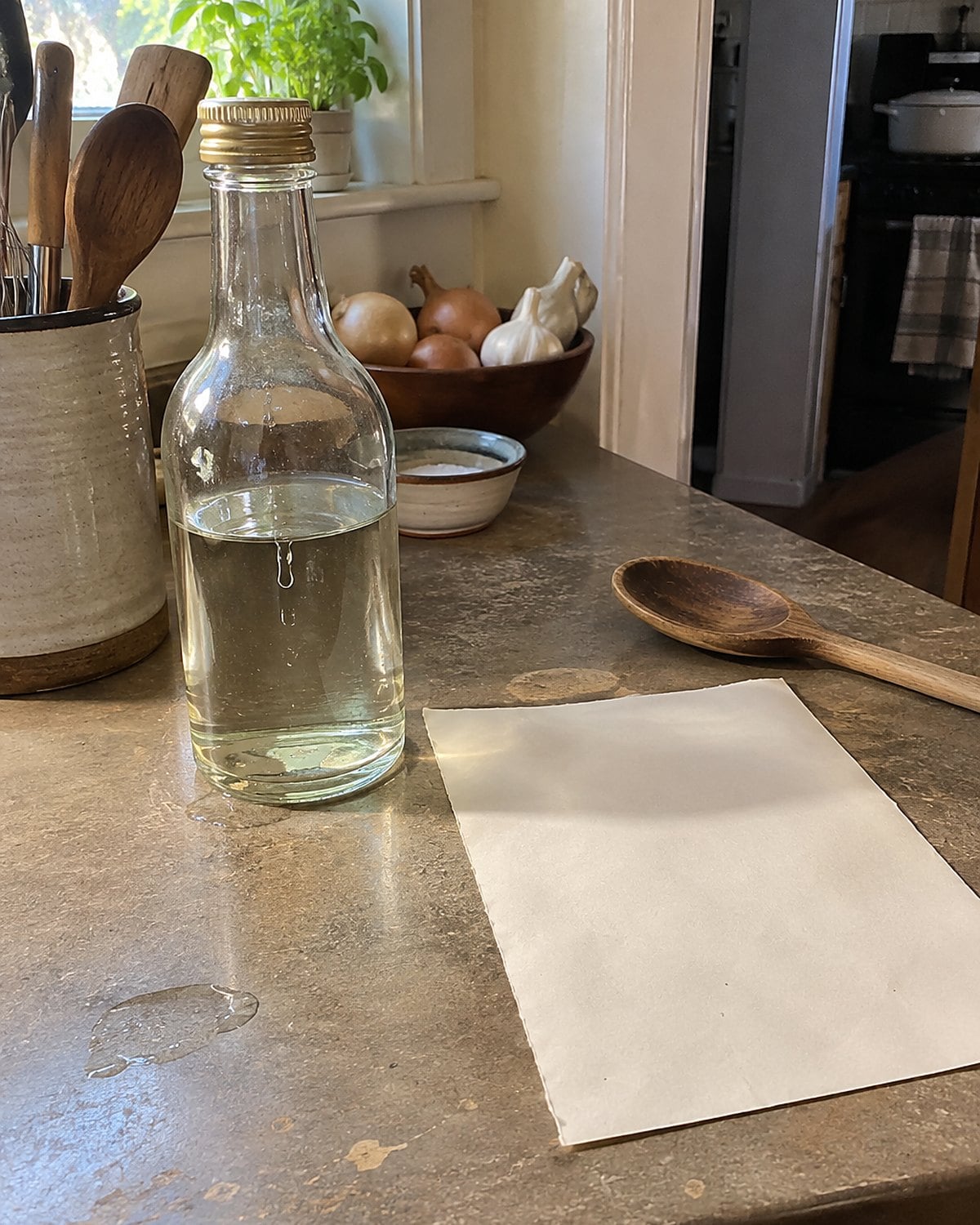 A vinegar bottle beside an old handwritten crust recipe on a pantry counter.