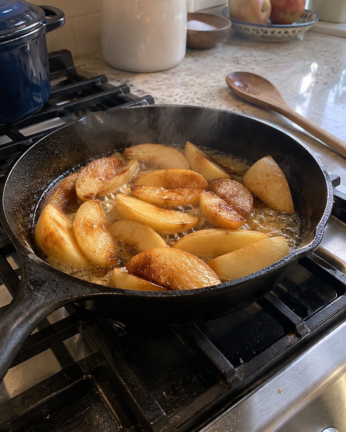 Apple wedges brown in a cast-iron pan on a home stove.