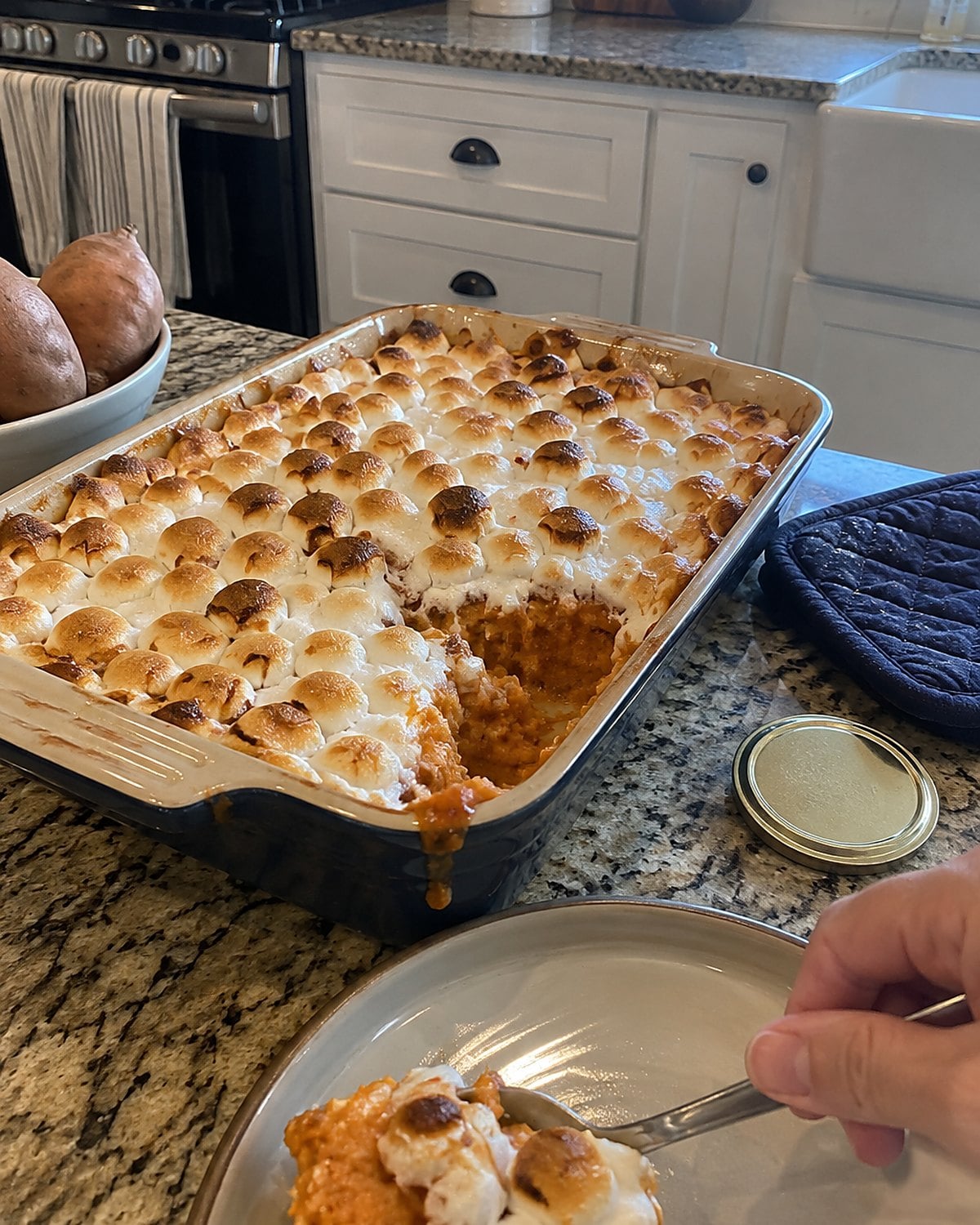 A baking dish of sweet potatoes with browned marshmallows sits near an oven mitt.