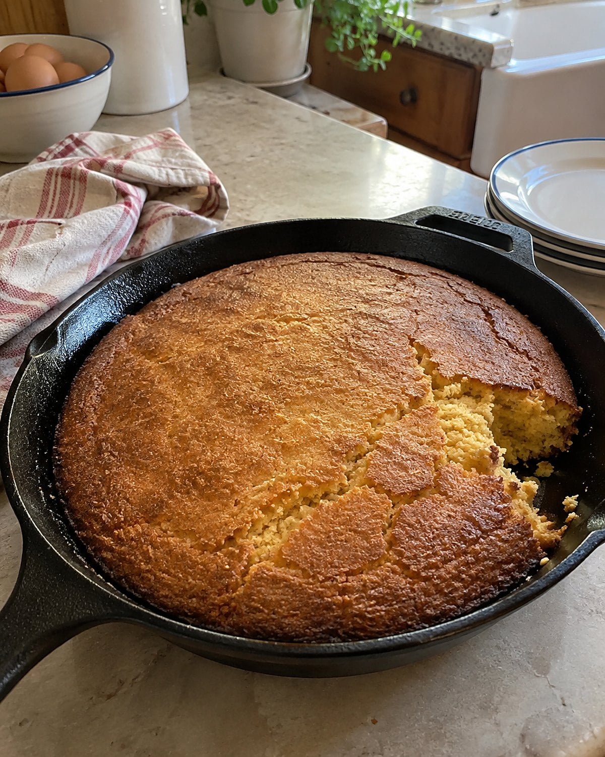 Cornbread with a dark crust rests in a cast-iron skillet on a kitchen counter.
