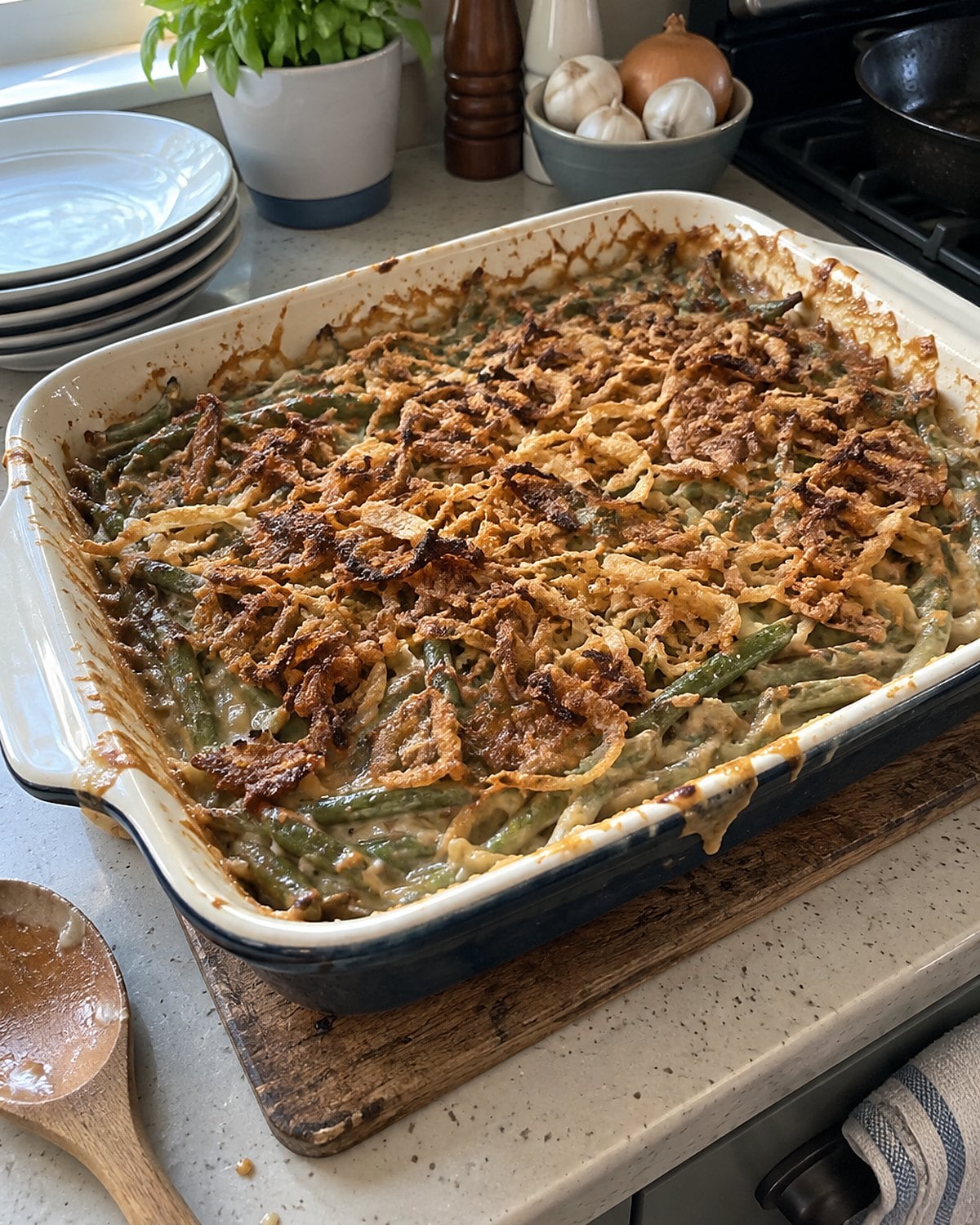 A green bean casserole with unevenly browned onions sits on a worn trivet beside the stove.
