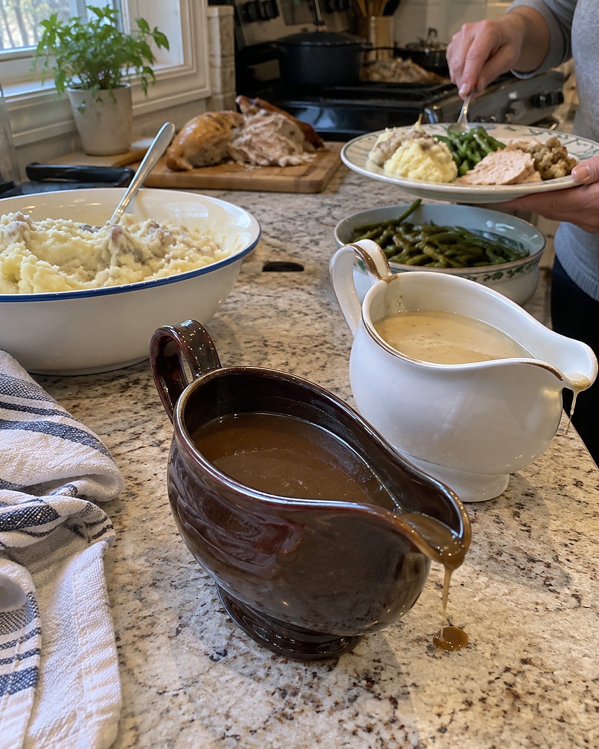 Two gravy boats, one pale and one dark, stand beside a bowl of potatoes.