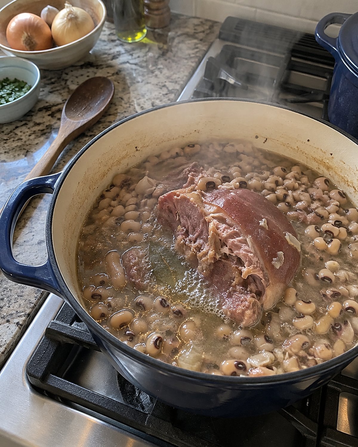 A ham hock and black-eyed peas simmer in a pot beside a wooden spoon.