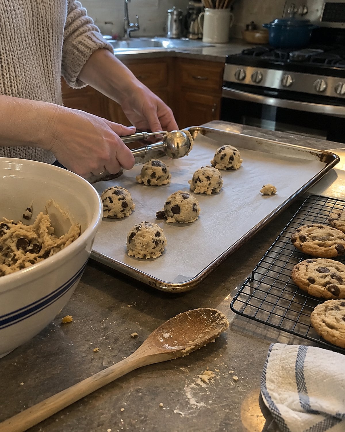 Uneven cookie dough portions sit on a baking sheet beside a cooling rack.