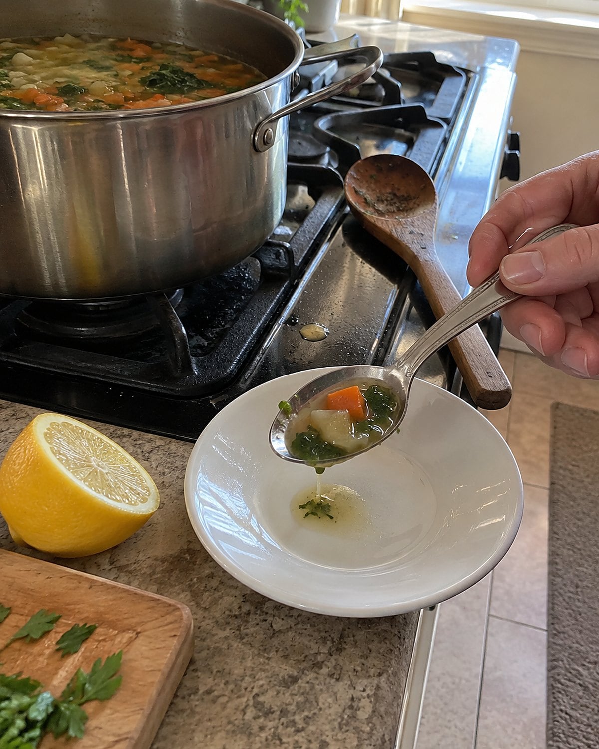A spoonful of vegetable soup cools beside a lemon half and a simmering pot.