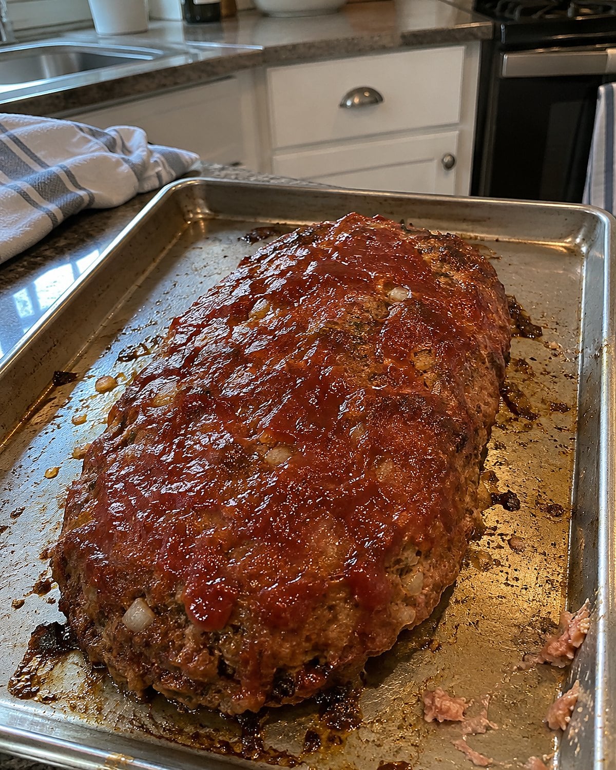 A hand-shaped meatloaf rests on a rimmed baking sheet with uneven edges and room around its sides.