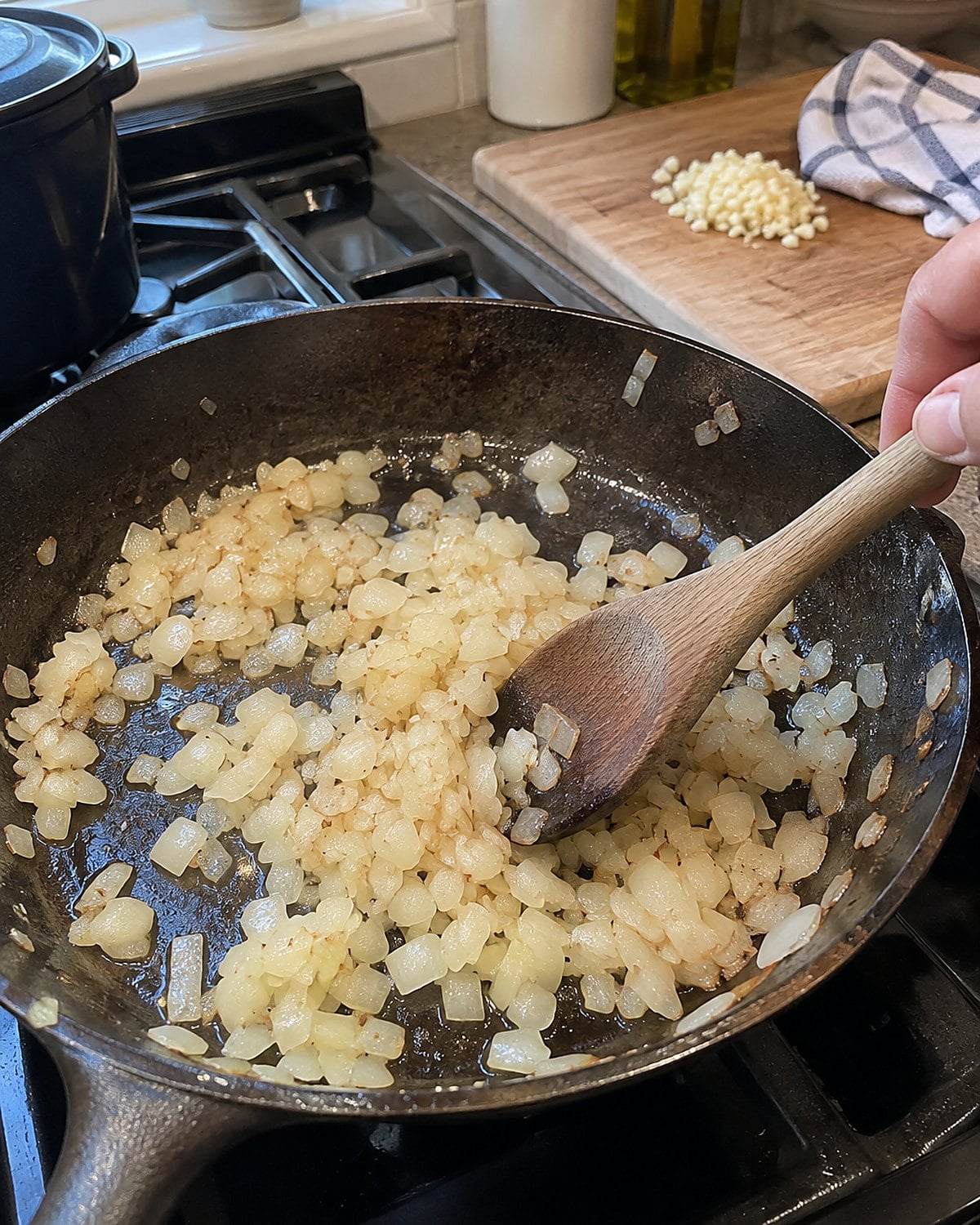 Chopped onion softens in a skillet beside a small pile of garlic waiting on the cutting board.