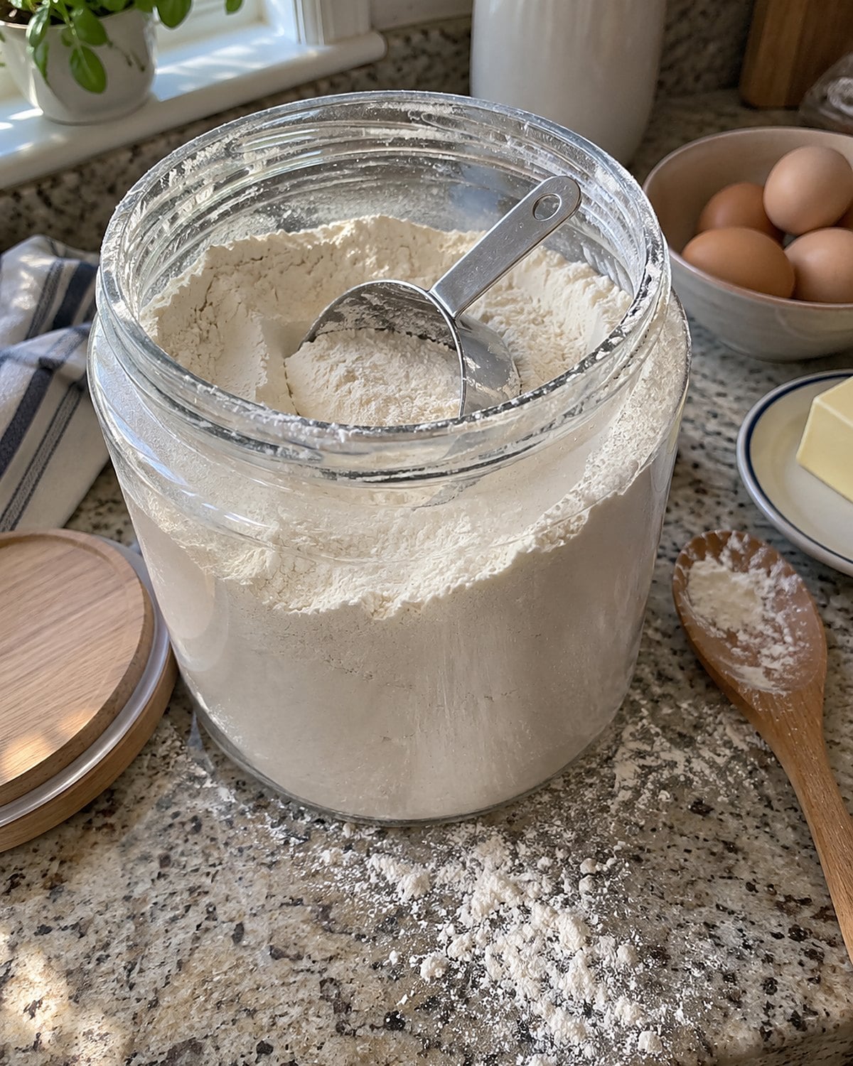 A metal measuring cup lies half-buried in an open flour canister on a kitchen counter.