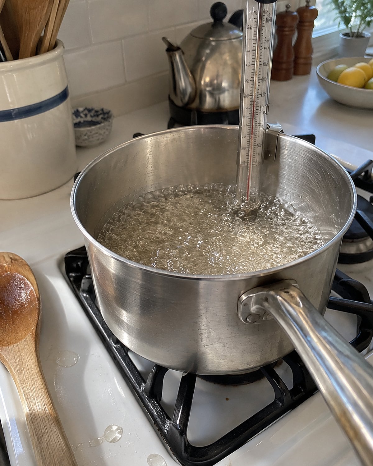A candy thermometer clips to a saucepan of bubbling water, its tip clear of the pot's bottom.