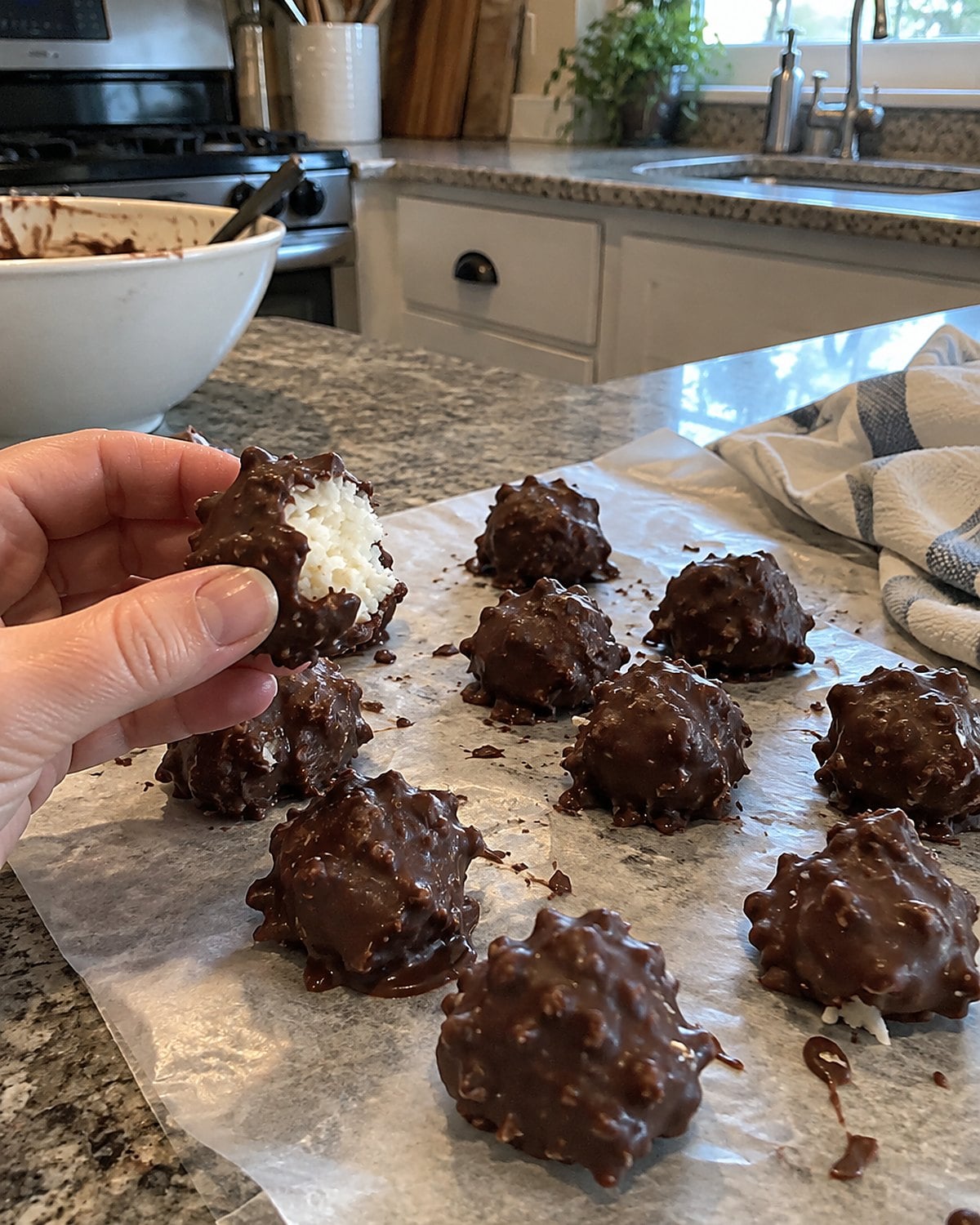 Uneven coconut bonbons set on wax paper, one showing a white patch beneath its chocolate.