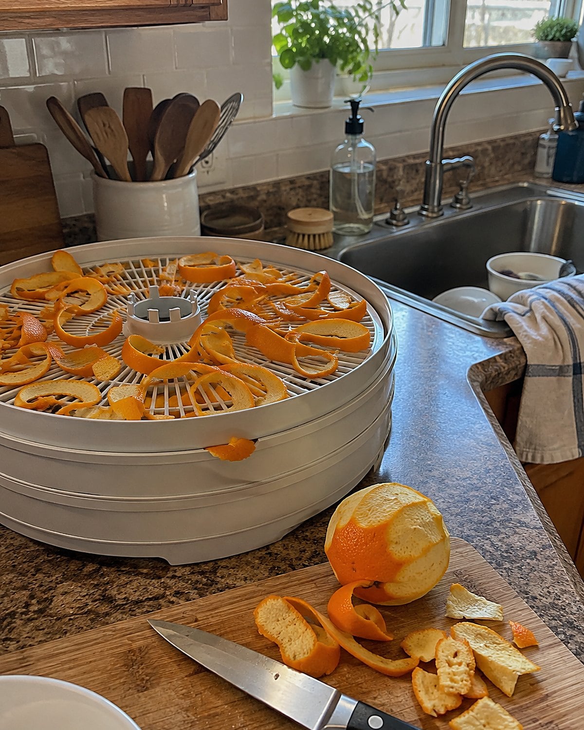 Orange peel strips dry on a rack by the sink, with trimmed peels and a knife nearby.