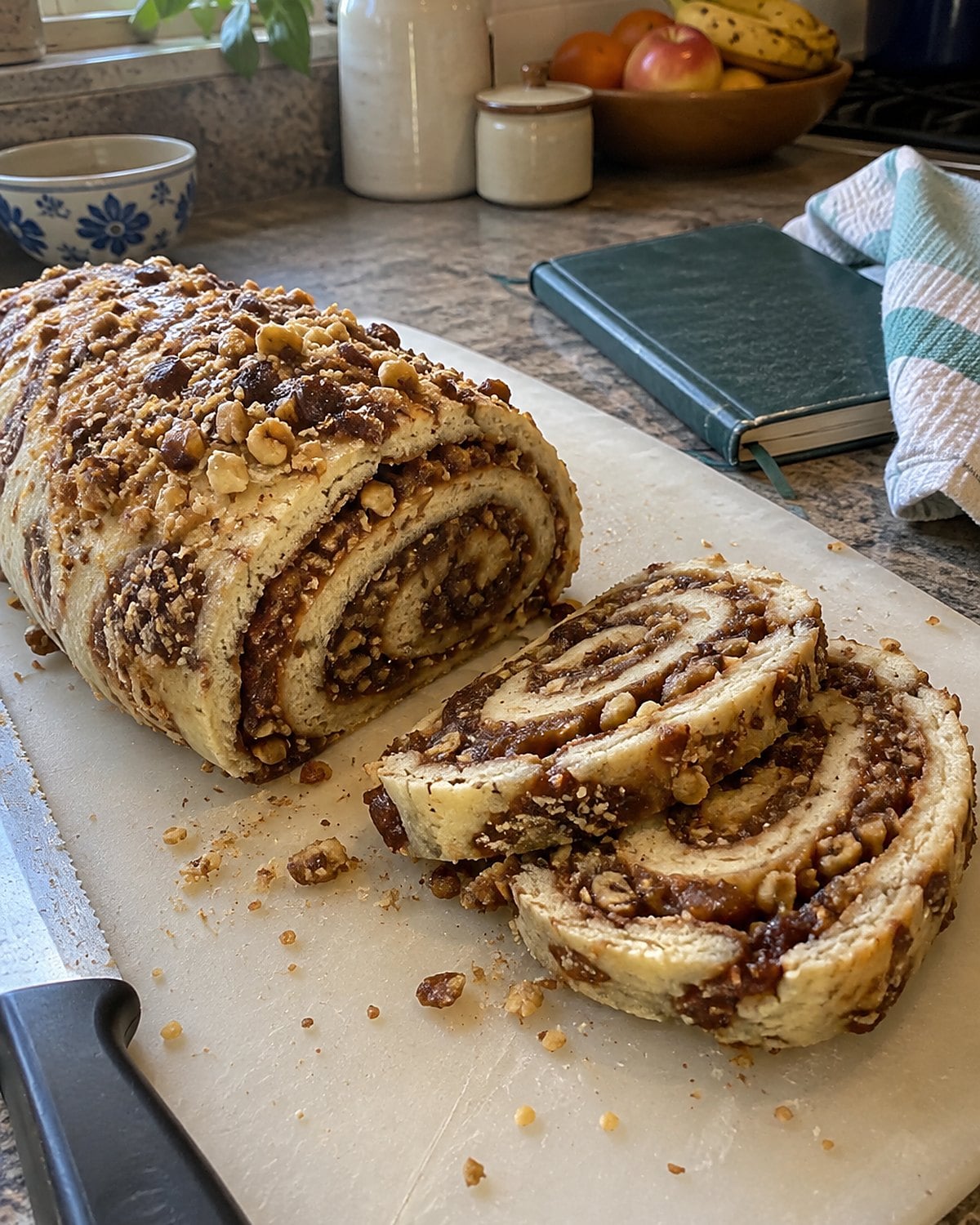 A cut date pinwheel sits beside an open, worn church cookbook on a busy kitchen counter.