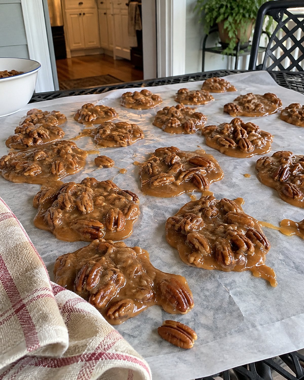 Pecan pralines set in uneven rounds on wax paper spread across a porch table.