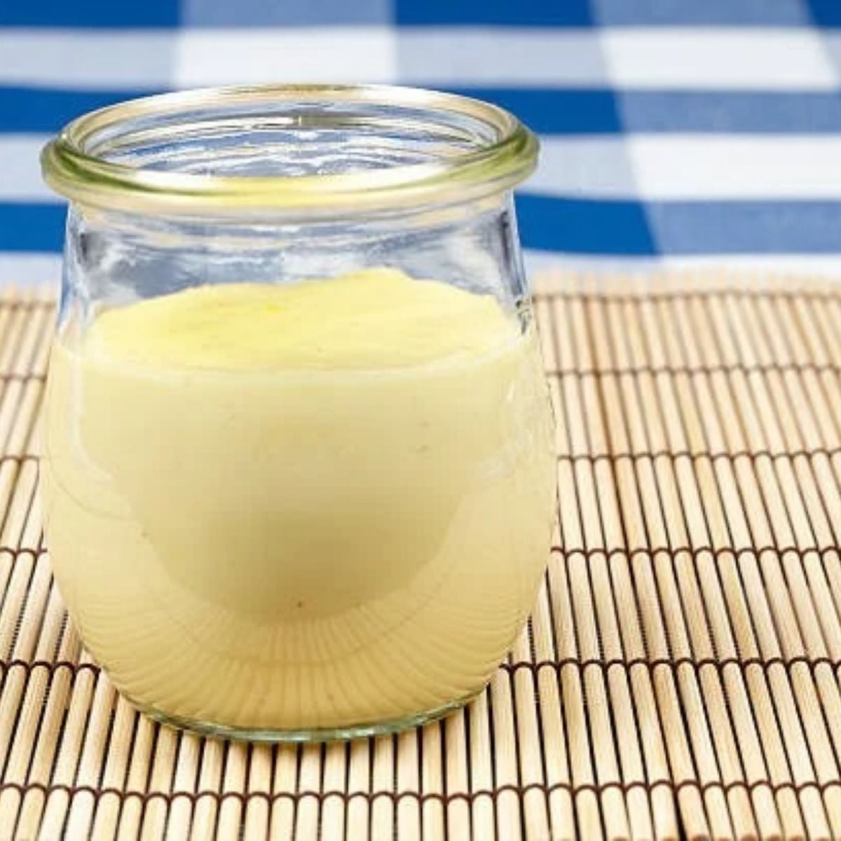 A small glass jar of homemade custard on a bamboo place mat on the counter