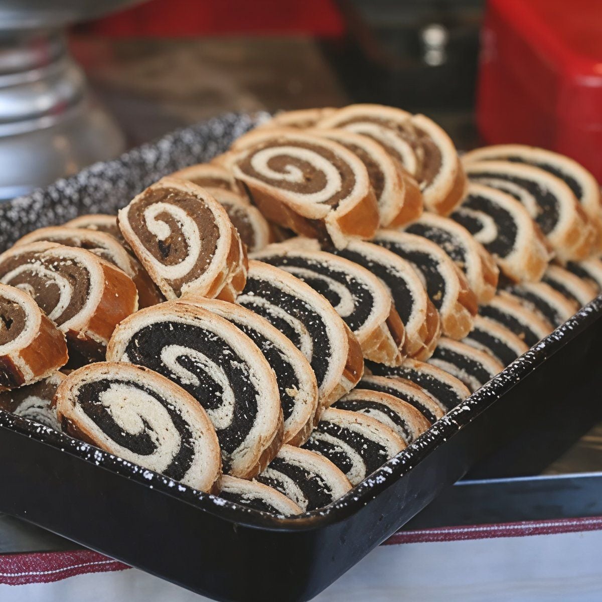 Slices of traditional Hungarian Bejgli roll cake displaying spiraled layers of poppy seed and walnut fillings arranged in a baking tray, served as a classic European Christmas dessert.