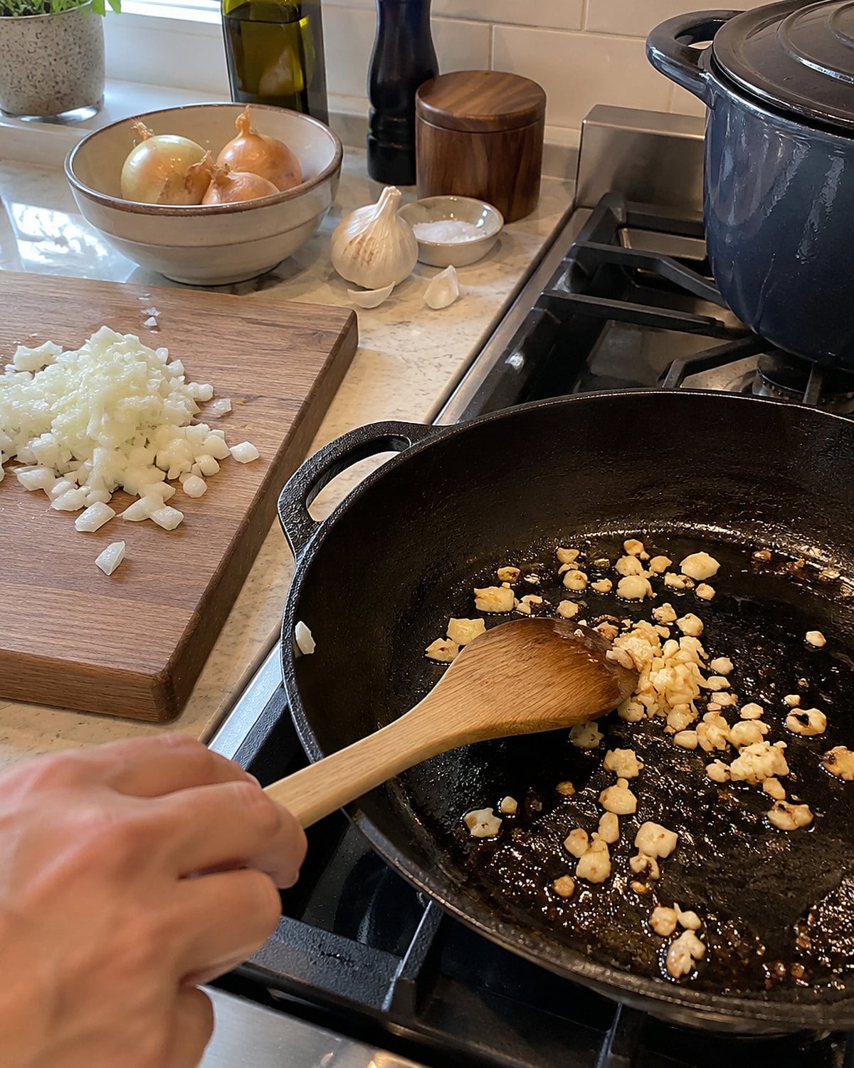 Chopped garlic darkens in a skillet beside an unfinished pile of diced onion.