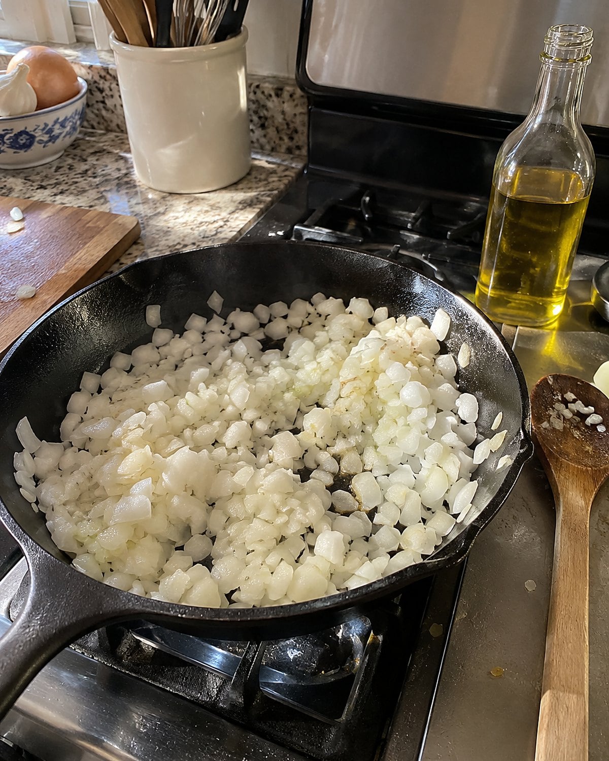 Chopped onion sits in a skillet on a home stove beside an uncapped bottle of oil.