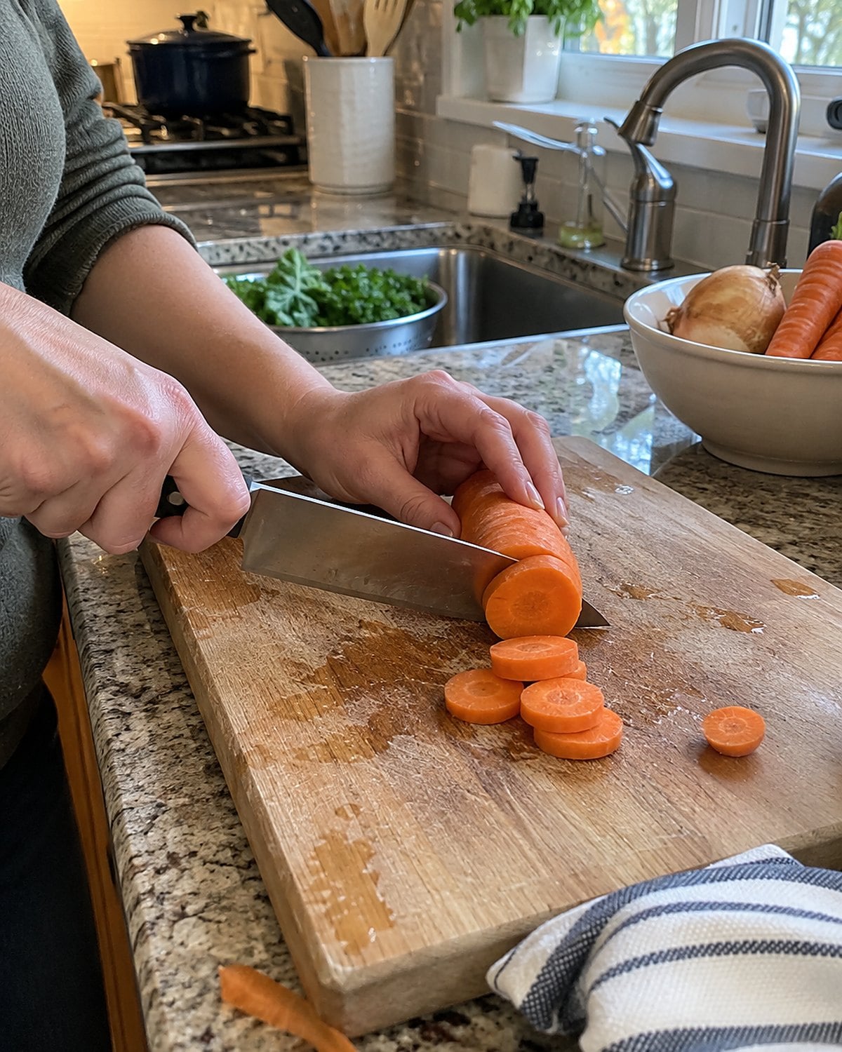 A kitchen knife lies on a damp cutting board beside a half-cut carrot and a folded towel.
