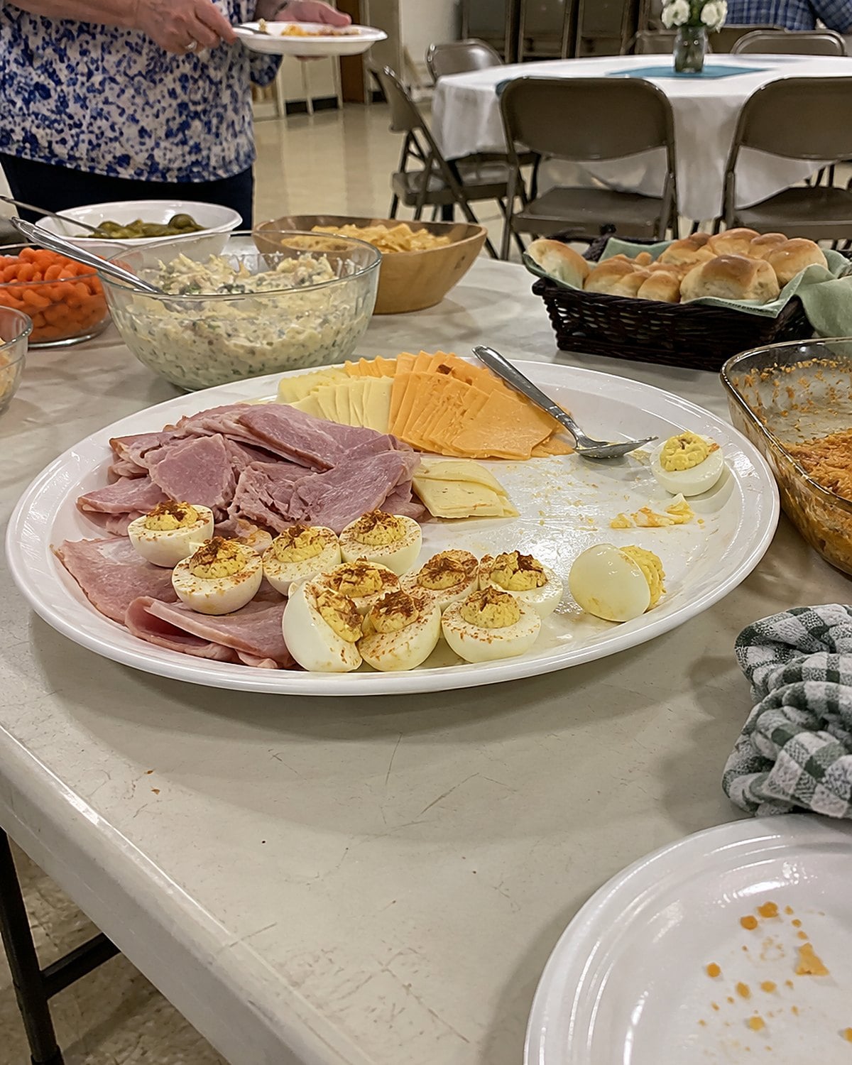 A partly eaten platter of ham, cheese, and deviled eggs on a church hall table after a gathering.