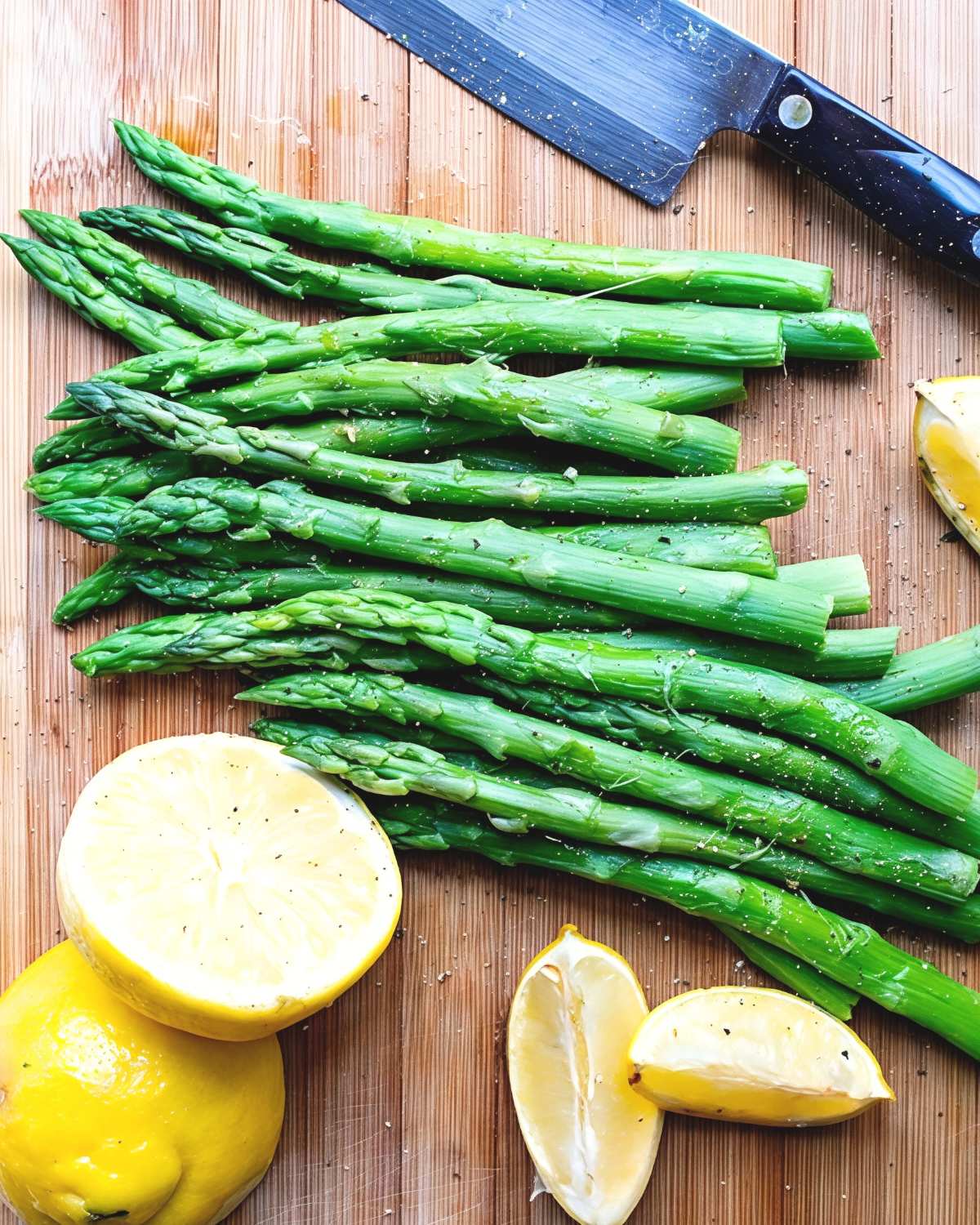 Freshly cooked Instant Pot asparagus with garlic, lemon wedges, and black pepper arranged on a cutting board, perfect for Thanksgiving side dishes for a crowd.