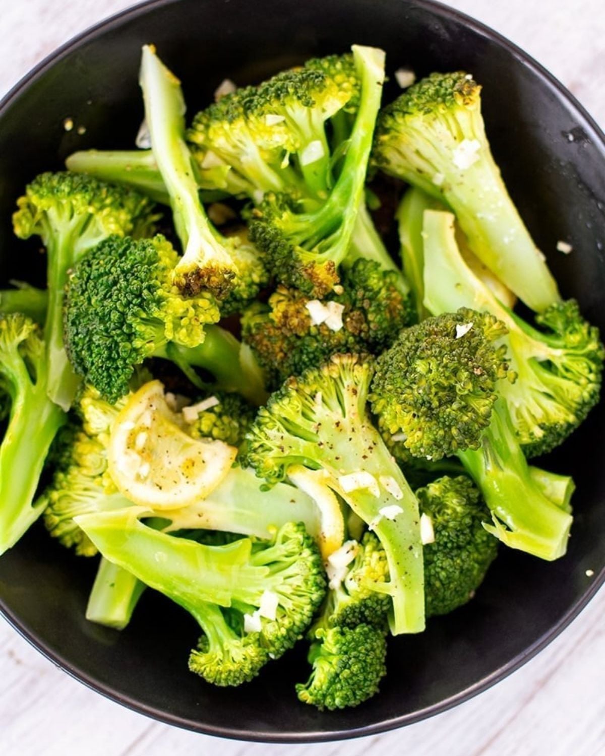 Instant Pot broccoli with lemon and garlic tossed in a dark bowl as a healthy vegan Thanksgiving side dish.