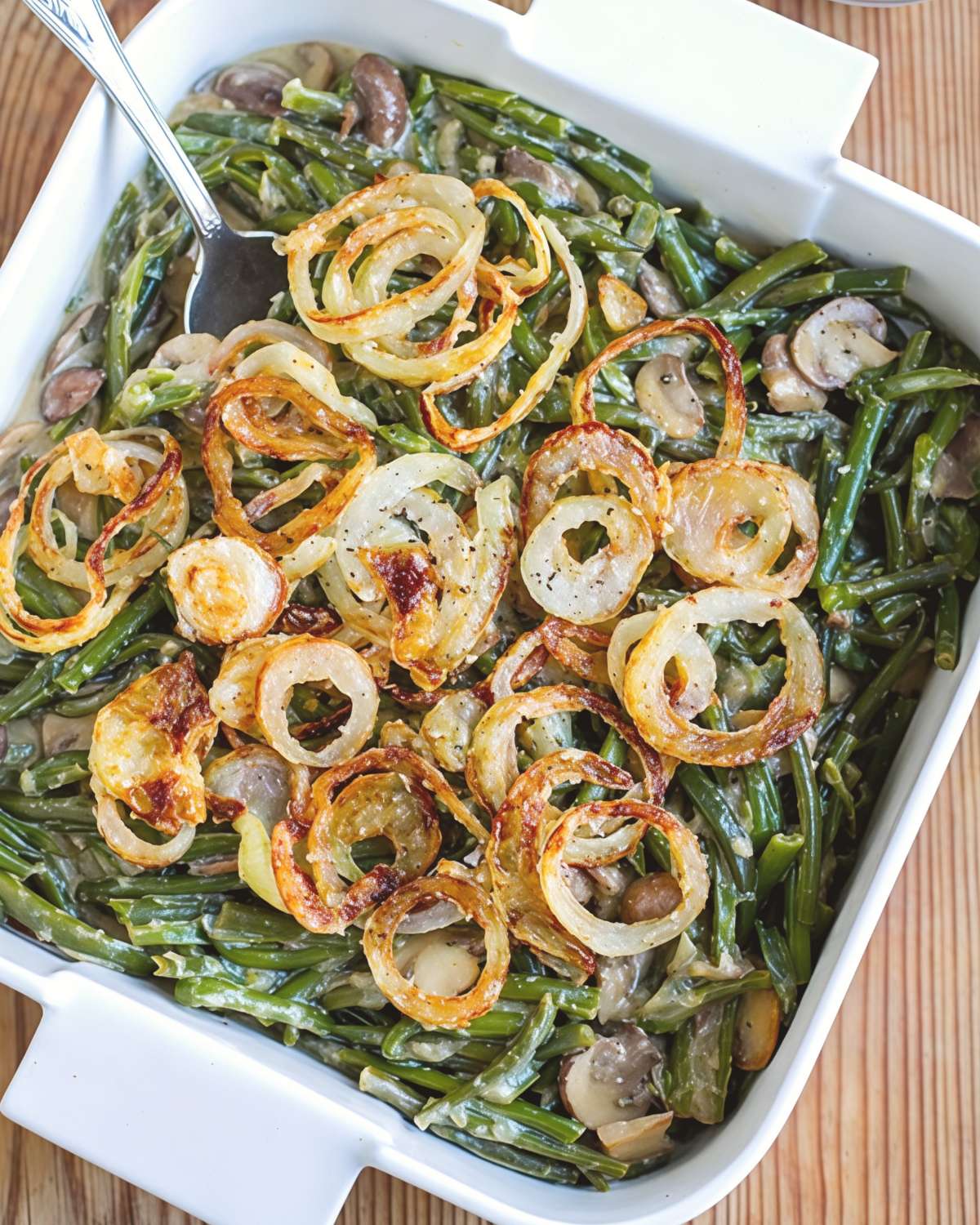 A white square baking dish filled with creamy green bean and mushroom casserole topped with crispy golden fried onion rings