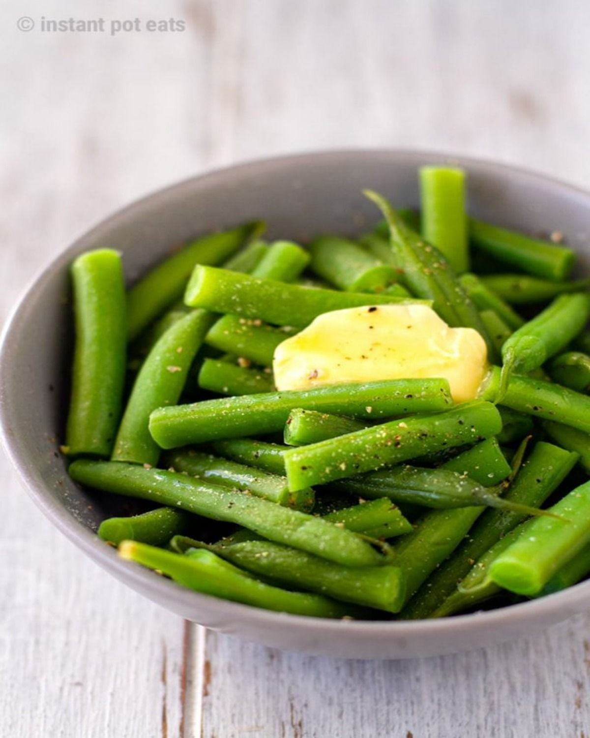 A bowl of tender Instant Pot green beans topped with melting butter and black pepper, perfect as easy Thanksgiving side dishes for a crowd.