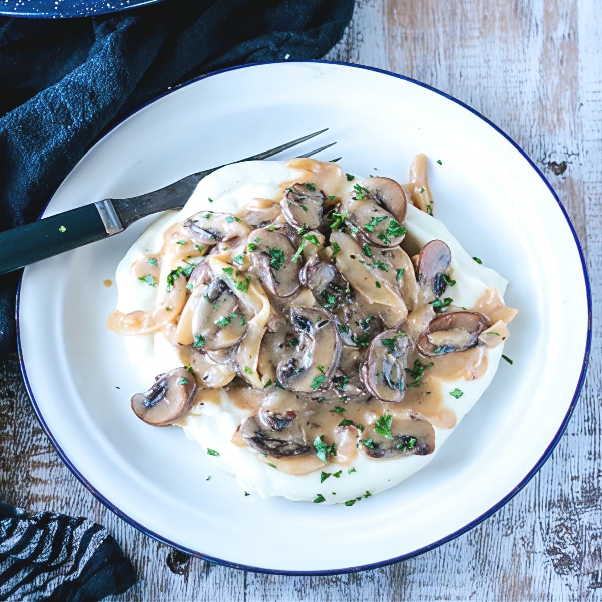A white enamel plate filled with tender Keto Salisbury Steak with Mushroom Gravy, featuring rich savory sauce and sliced mushrooms sprinkled with fresh parsley over low-carb mash, featured as a delicious high protein low carb recipes dinner.