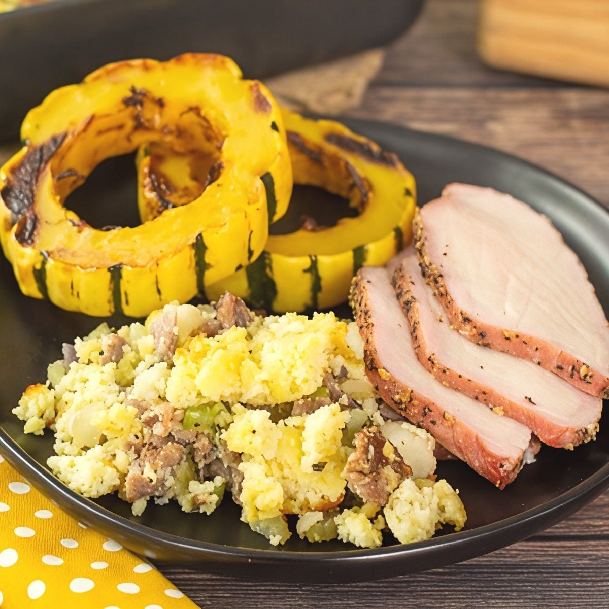 Savory keto sausage stuffing served alongside roasted acorn squash rings and sliced pork loin on a dark plate, making a perfect addition to keto thanksgiving sides.