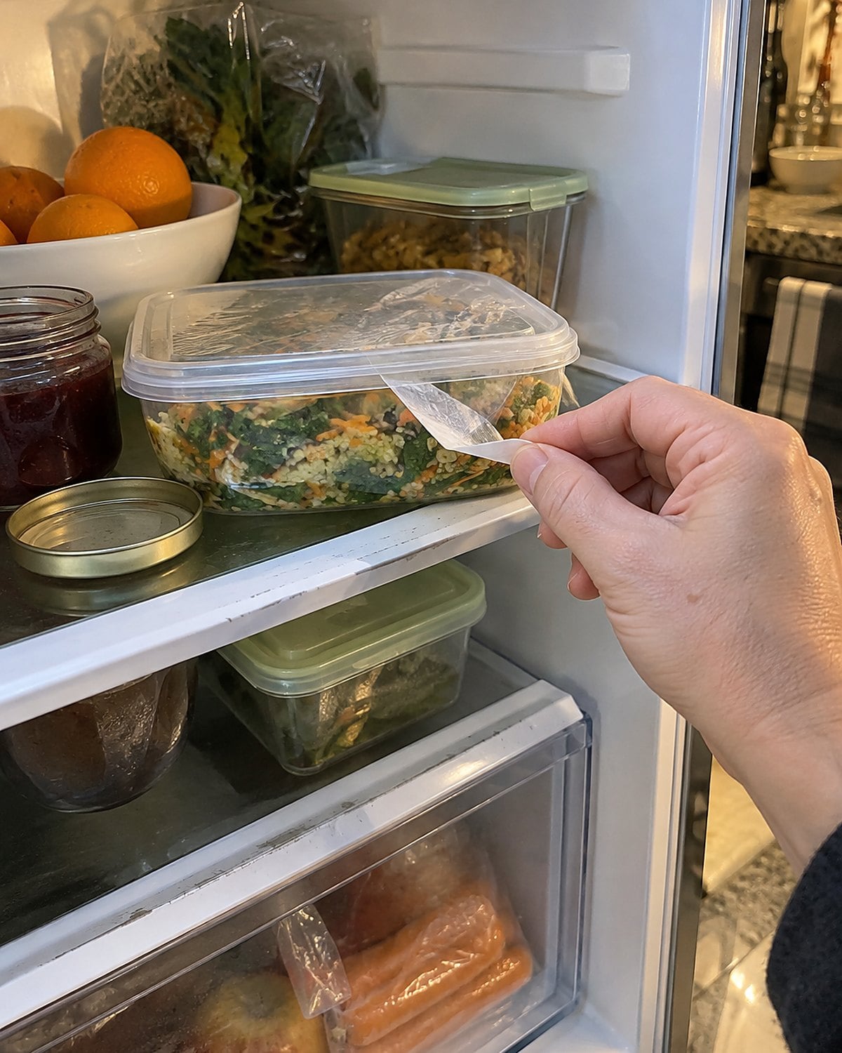 A curled tape label peeling from a plastic food container on a fridge shelf.
