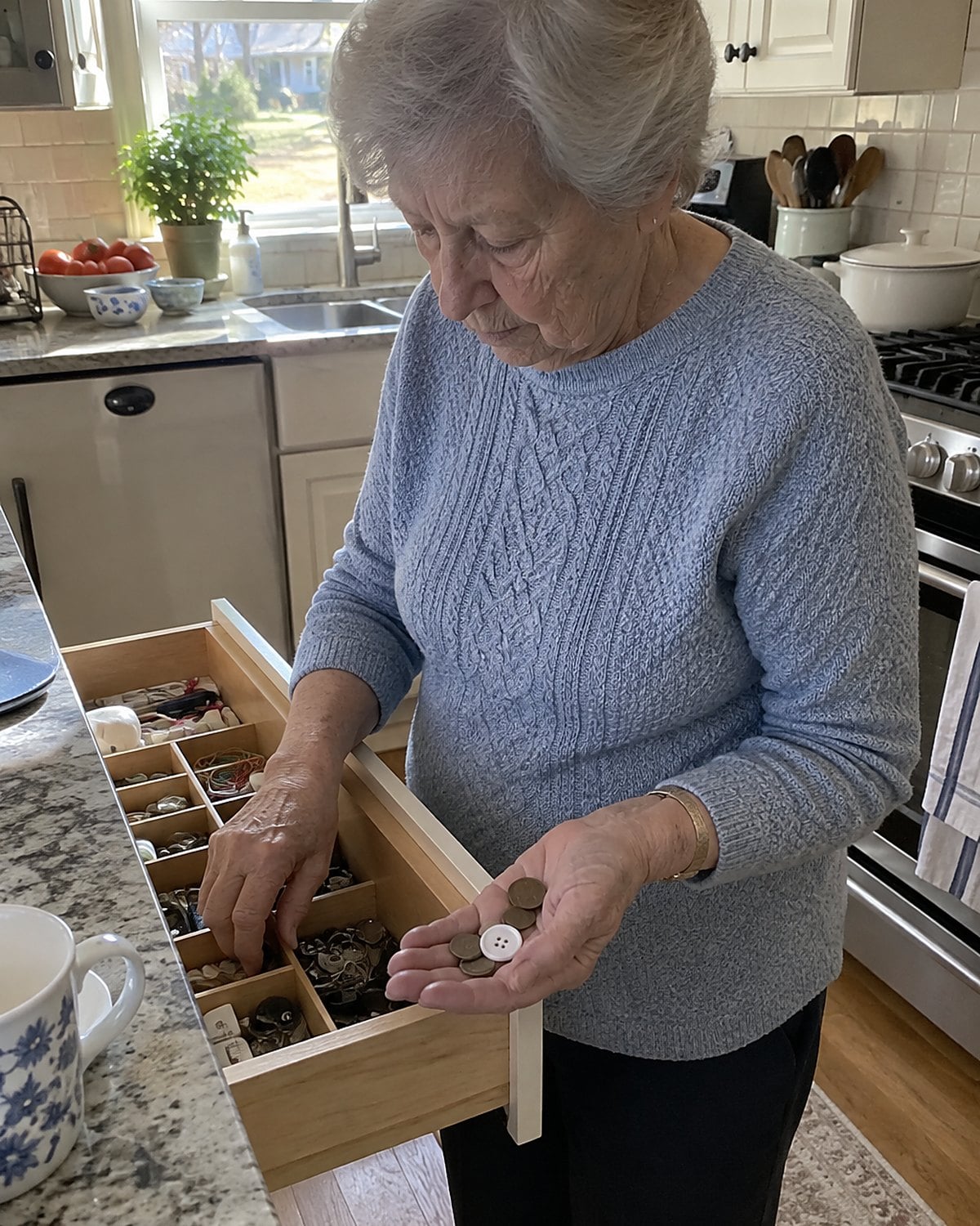 A loose button and a few coins in an older womanโs palm above an open kitchen drawer.