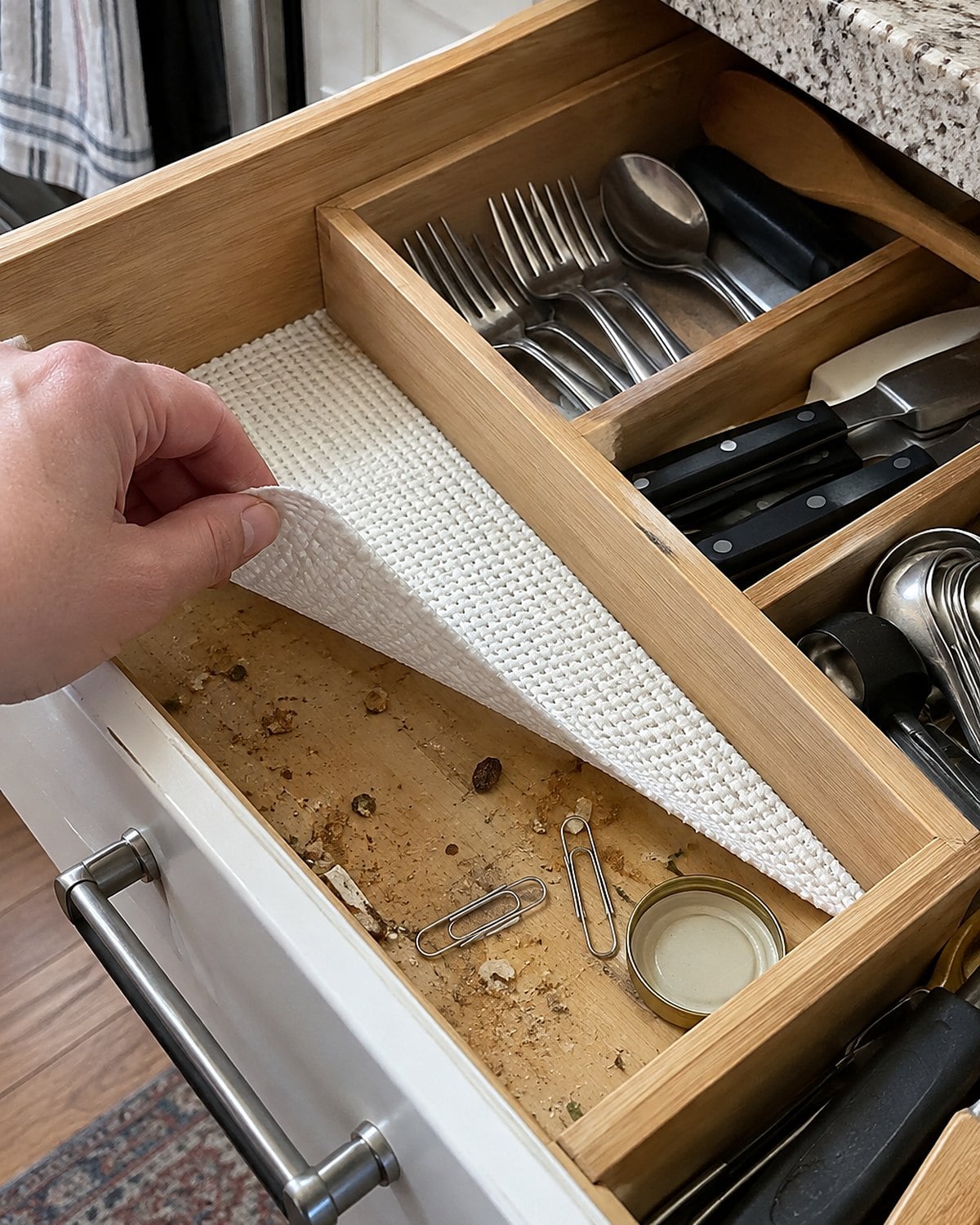 Bent paper clips and crumbs exposed beneath a lifted drawer liner.
