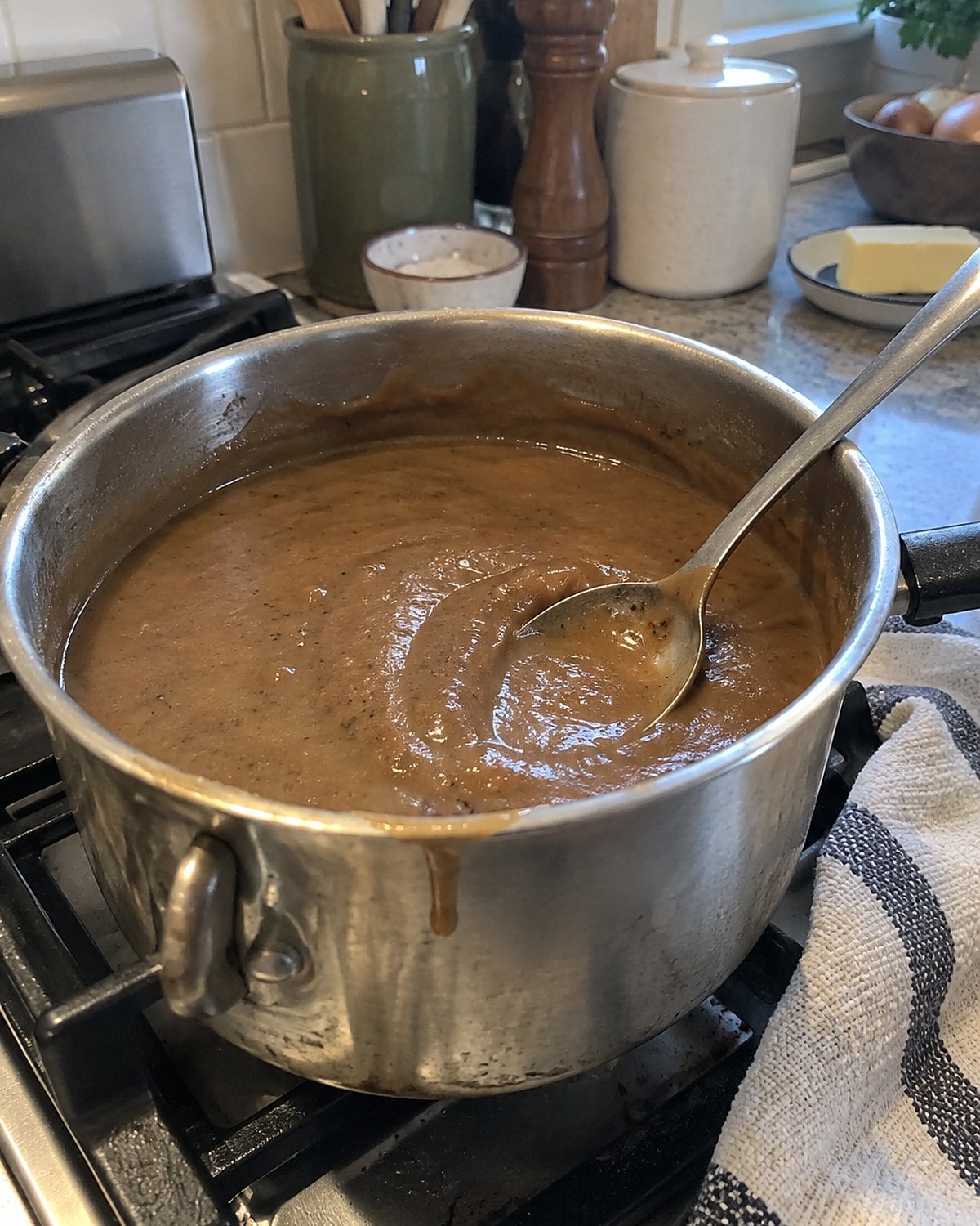 A spoon drags through thick gravy in a small saucepan on the stove.