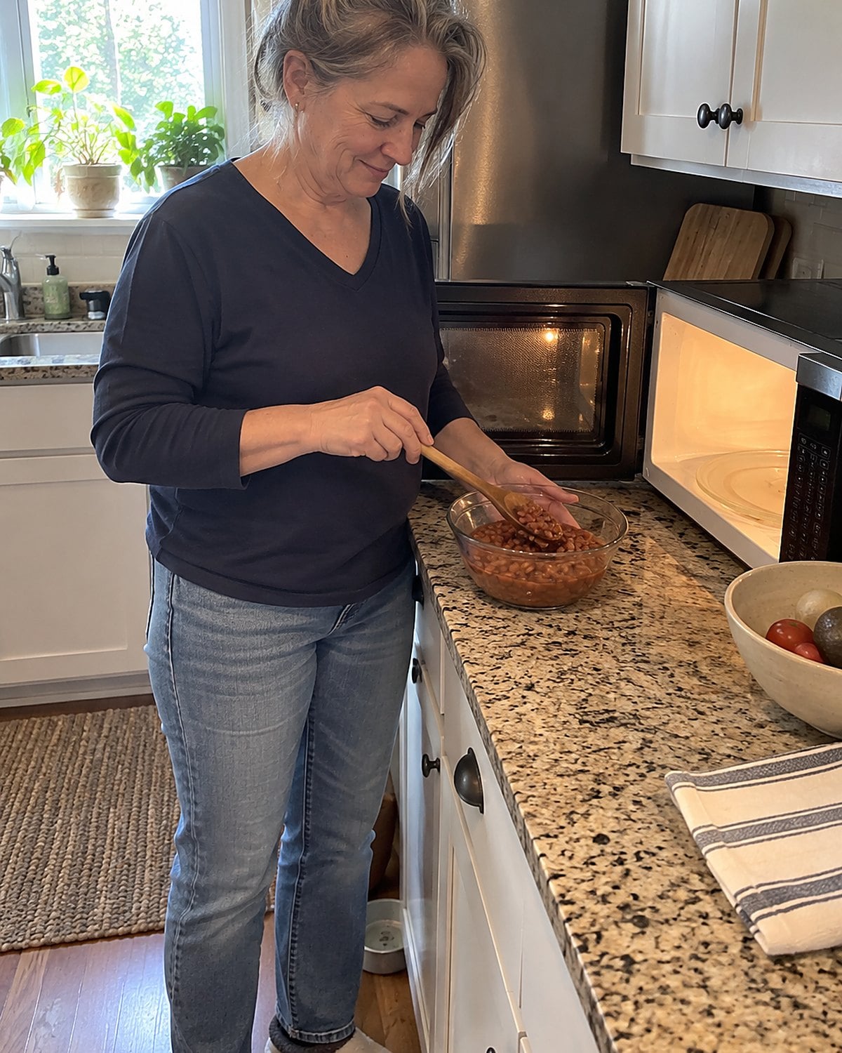 A hand stirs beans in a microwave-safe bowl beside an open microwave.