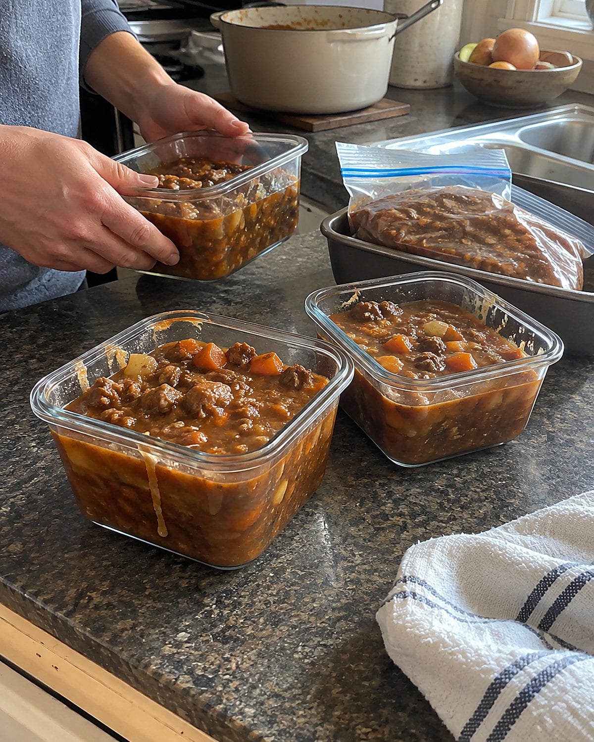A freezer bag rests in a tray beside shallow containers of cooling stew on the counter.