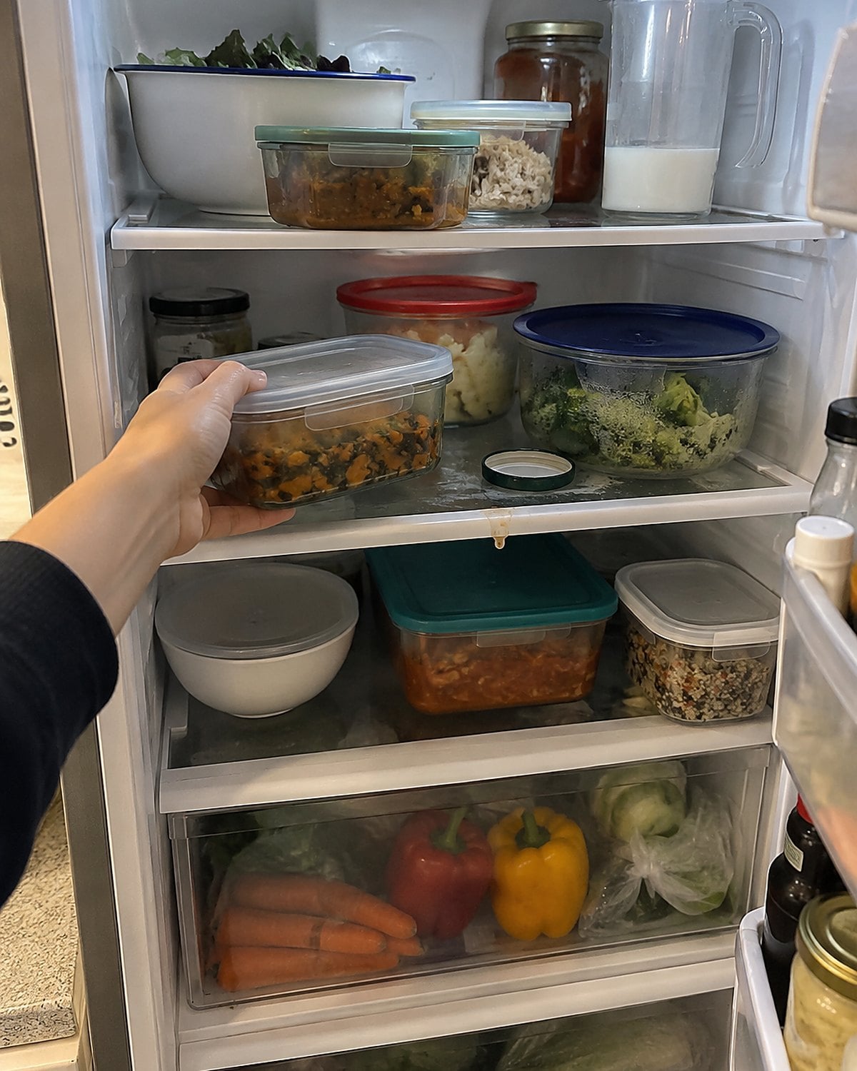 An open refrigerator shows containers of leftovers on the shelves.