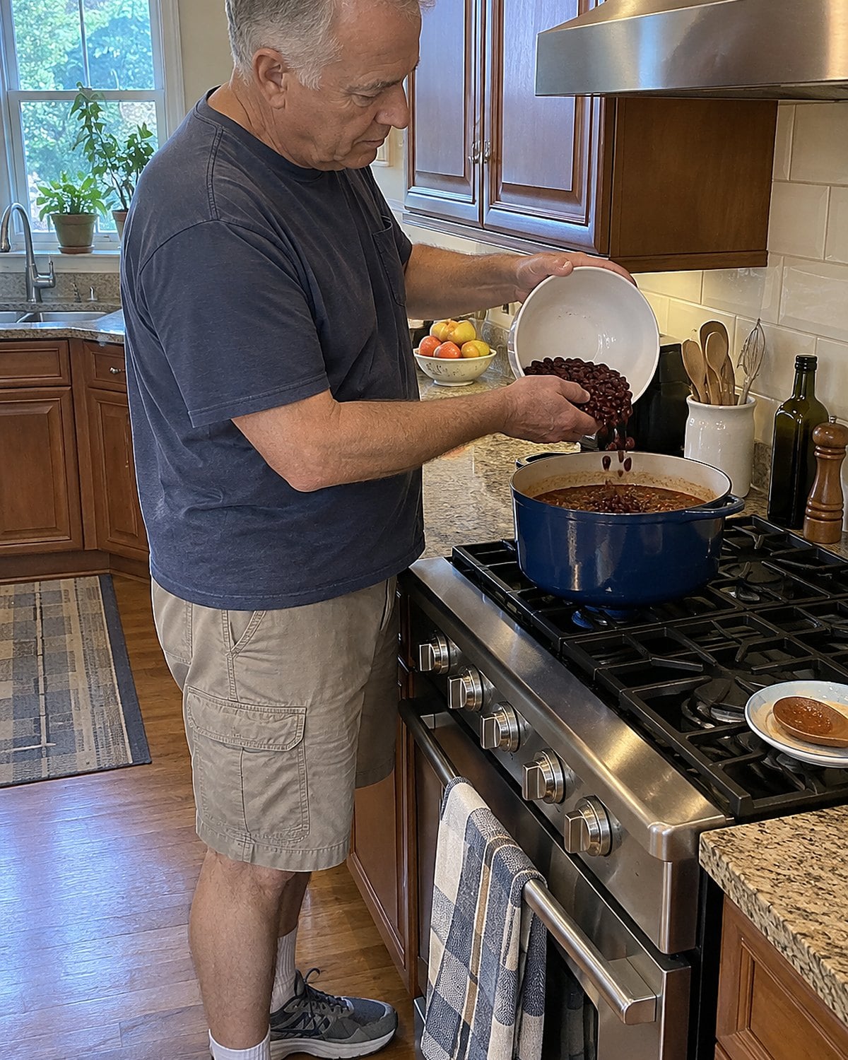 Hands tip fresh beans into a pot of leftover chili on the stove.