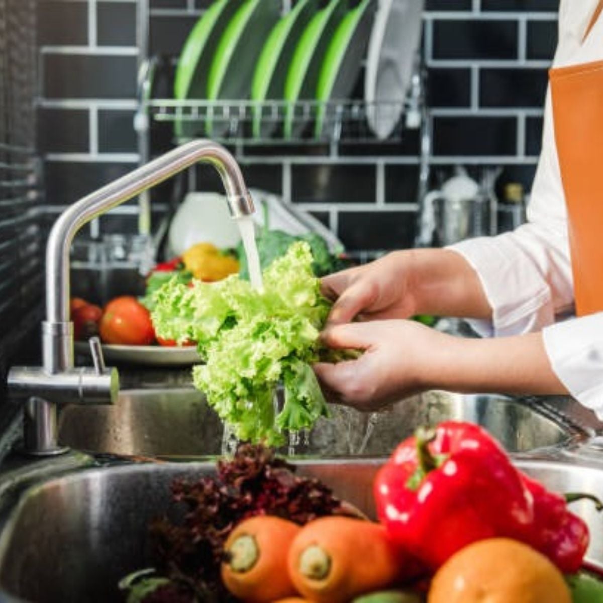 a person rinsing lettuce in the sink with other veggies laying in the water