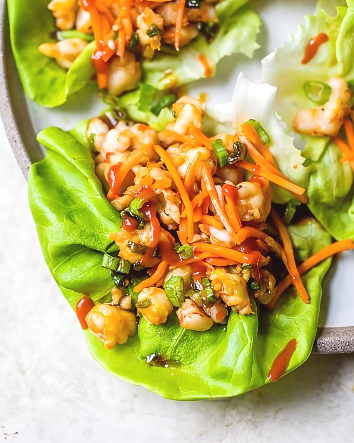 Close-up view of crisp green lettuce cups stuffed with sautรฉed minced shrimp, julienned carrots, scallions, and spicy sauce, featured as a delicious high protein low carb recipes dinner.