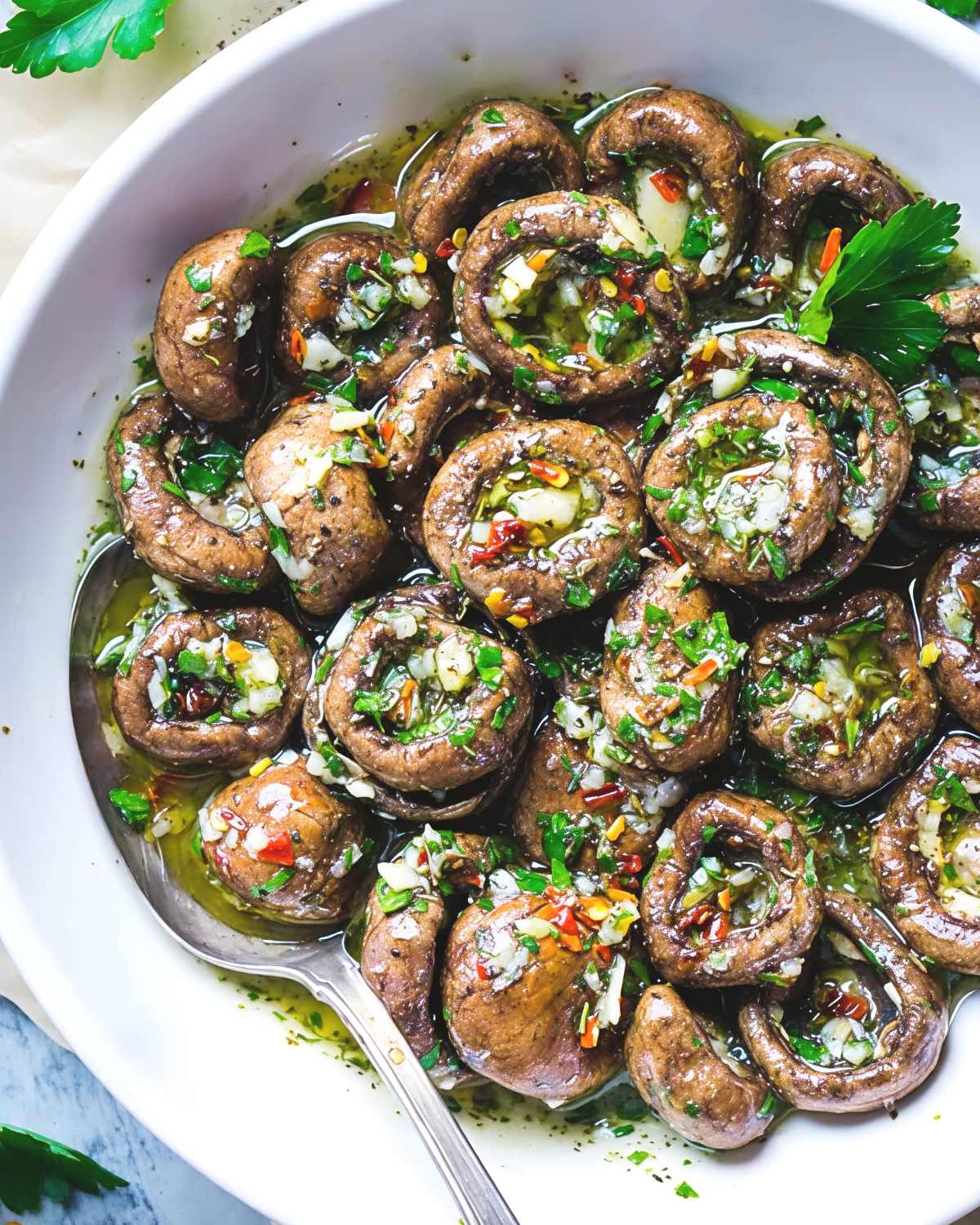 Savory marinated button mushrooms tossed in olive oil, minced garlic, herbs, and red pepper flakes served in a white bowl as a healthy, light Thanksgiving appetizer.