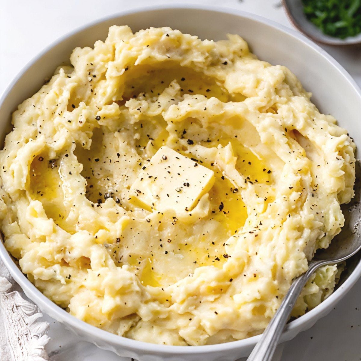 Creamy crockpot mashed potatoes topped with melted butter and cracked black pepper in a white bowl as crockpot thanksgiving sides.