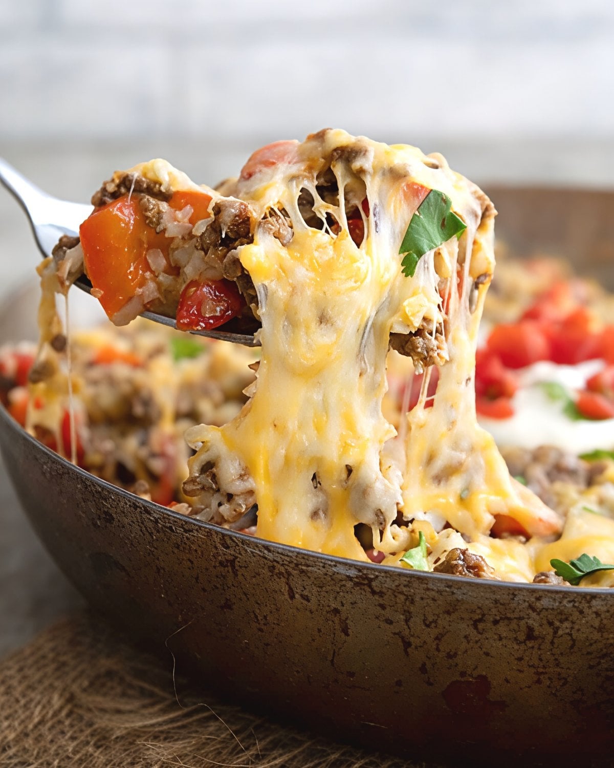 Close-up view of Mexican Cauliflower Rice skillet topped with gooey melted cheese, diced tomatoes, ground beef, and peppers, featured as a delicious high protein low carb recipes dinner.
