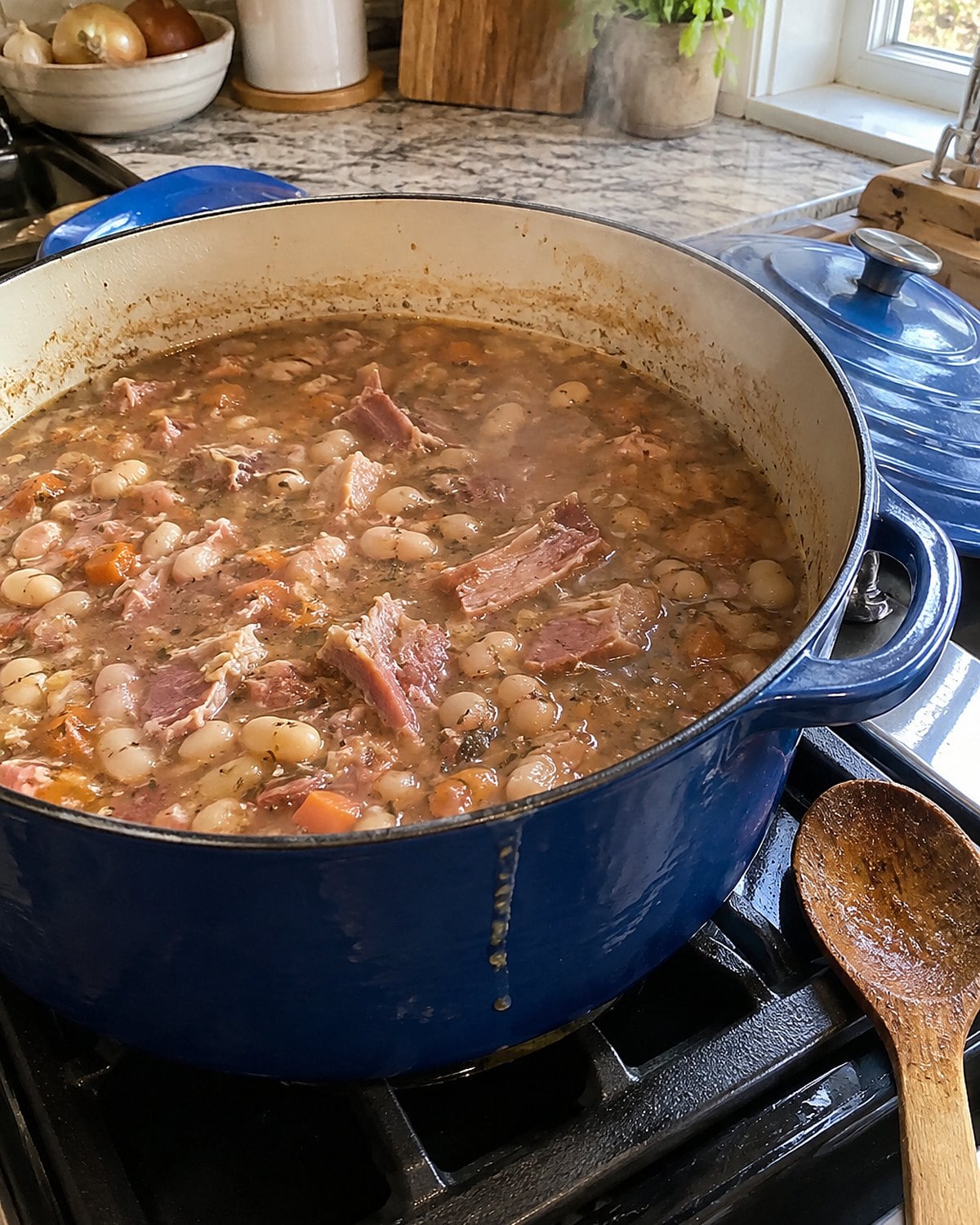 A Dutch oven of ham and beans with the lid propped beside it on the stove.