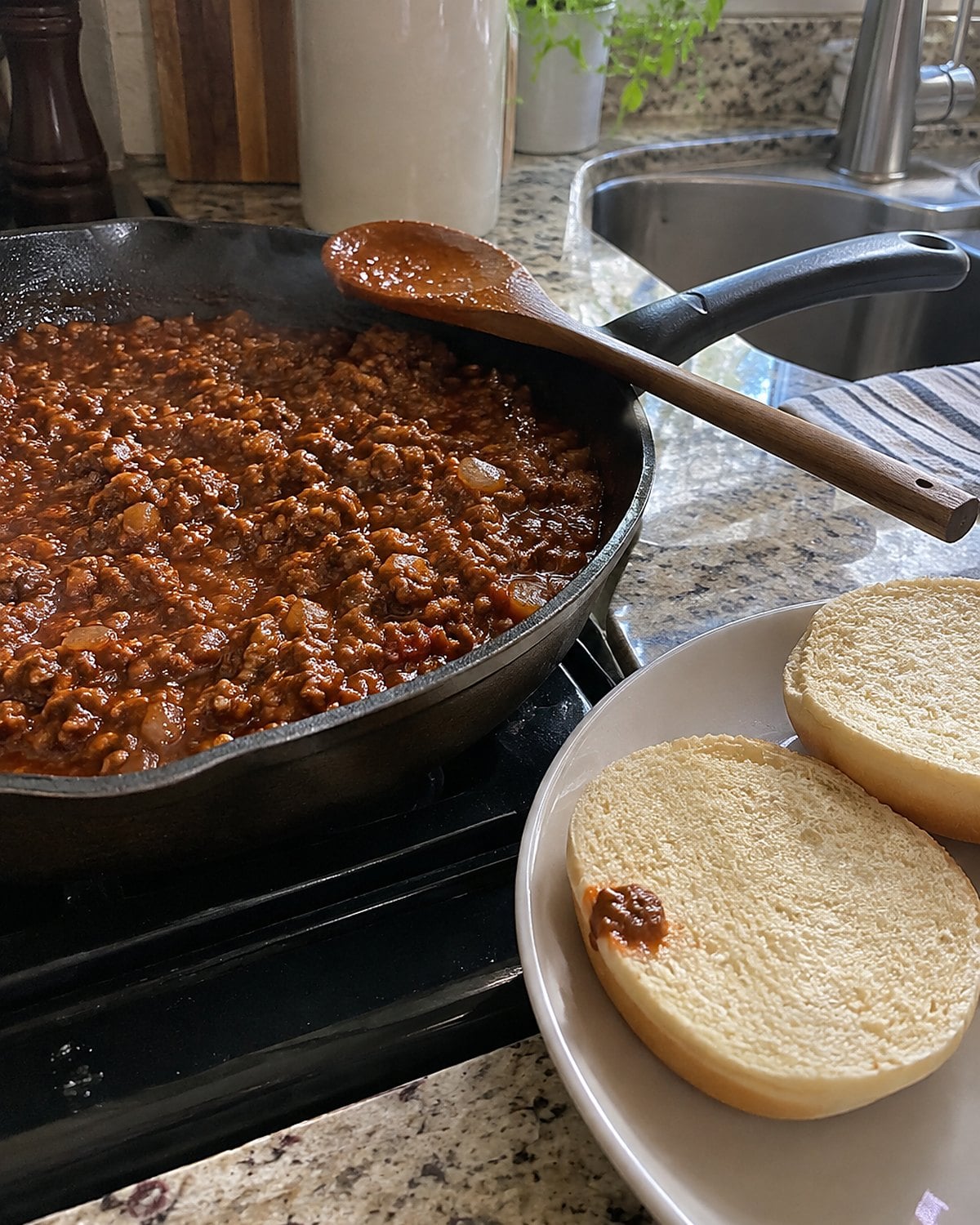 Sloppy joe filling thickening in a skillet beside two open buns.