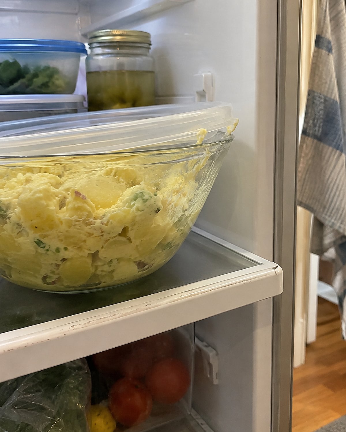 A yellow potato salad in a covered bowl on a refrigerator shelf.