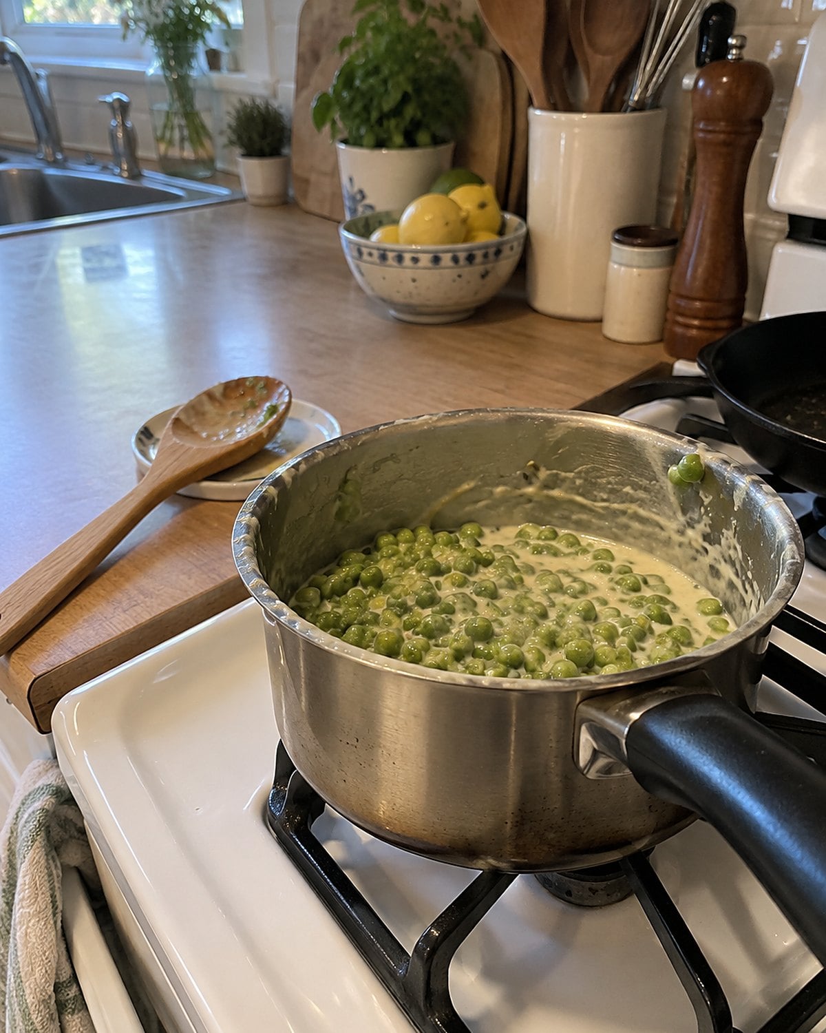 A small saucepan of creamed peas beside a wooden spoon on the stove.