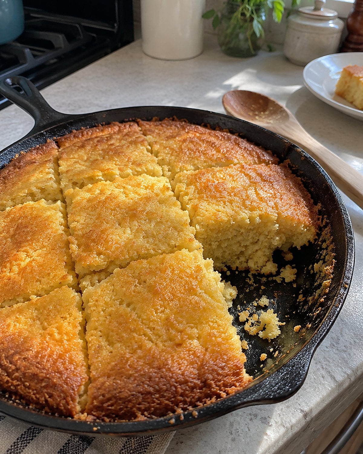 A cast-iron skillet of cornbread with a browned edge and one imperfect square cut.