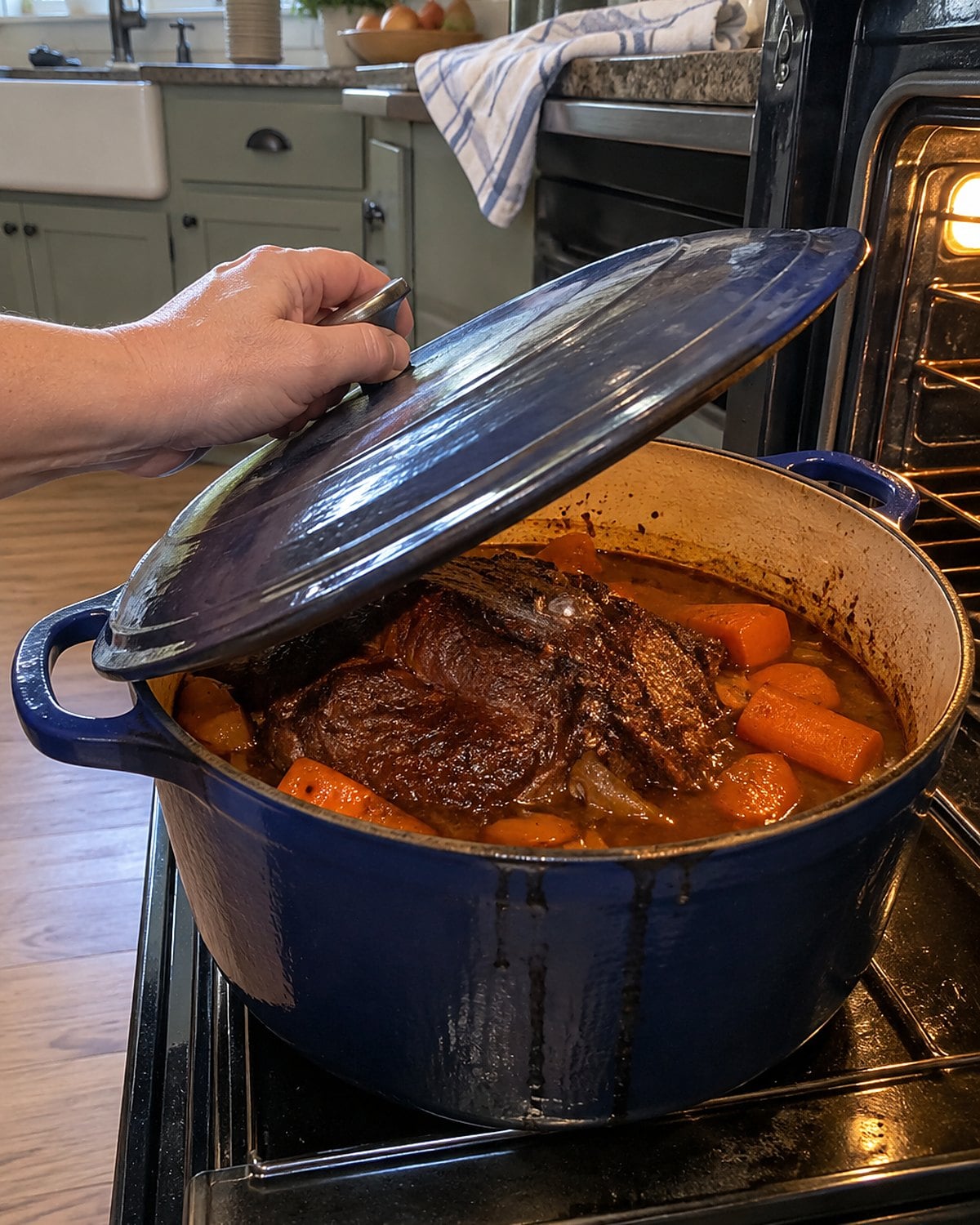 A pot roast with carrots in a heavy covered pot on an open oven door.