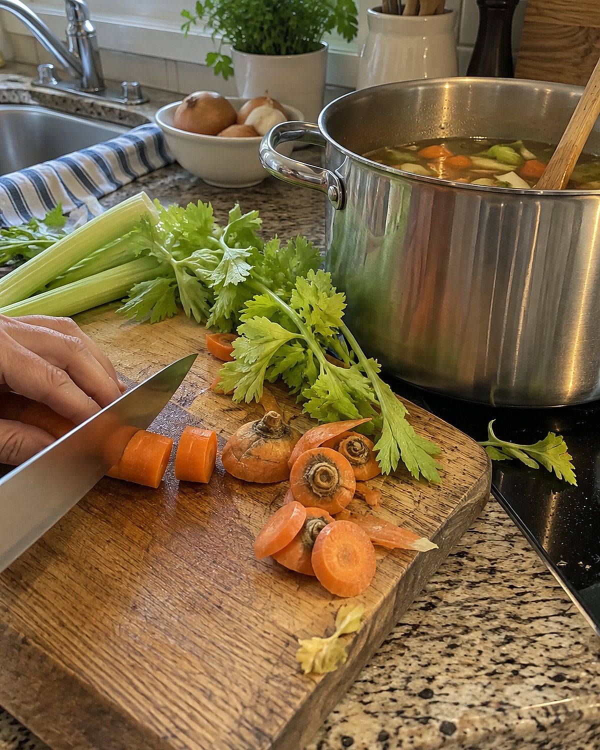 Carrot ends and celery leaves lie beside a stockpot on a worn cutting board.
