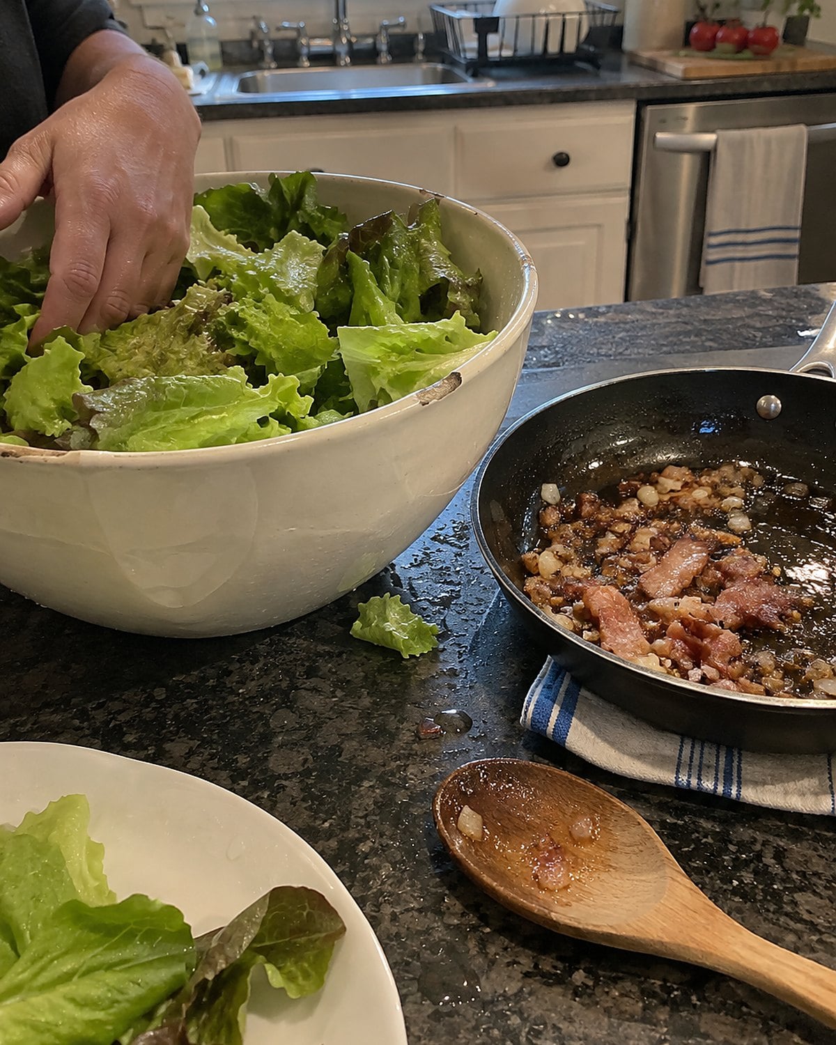 Washed lettuce leaves sit in a chipped bowl beside a small pan of bacon dressing.